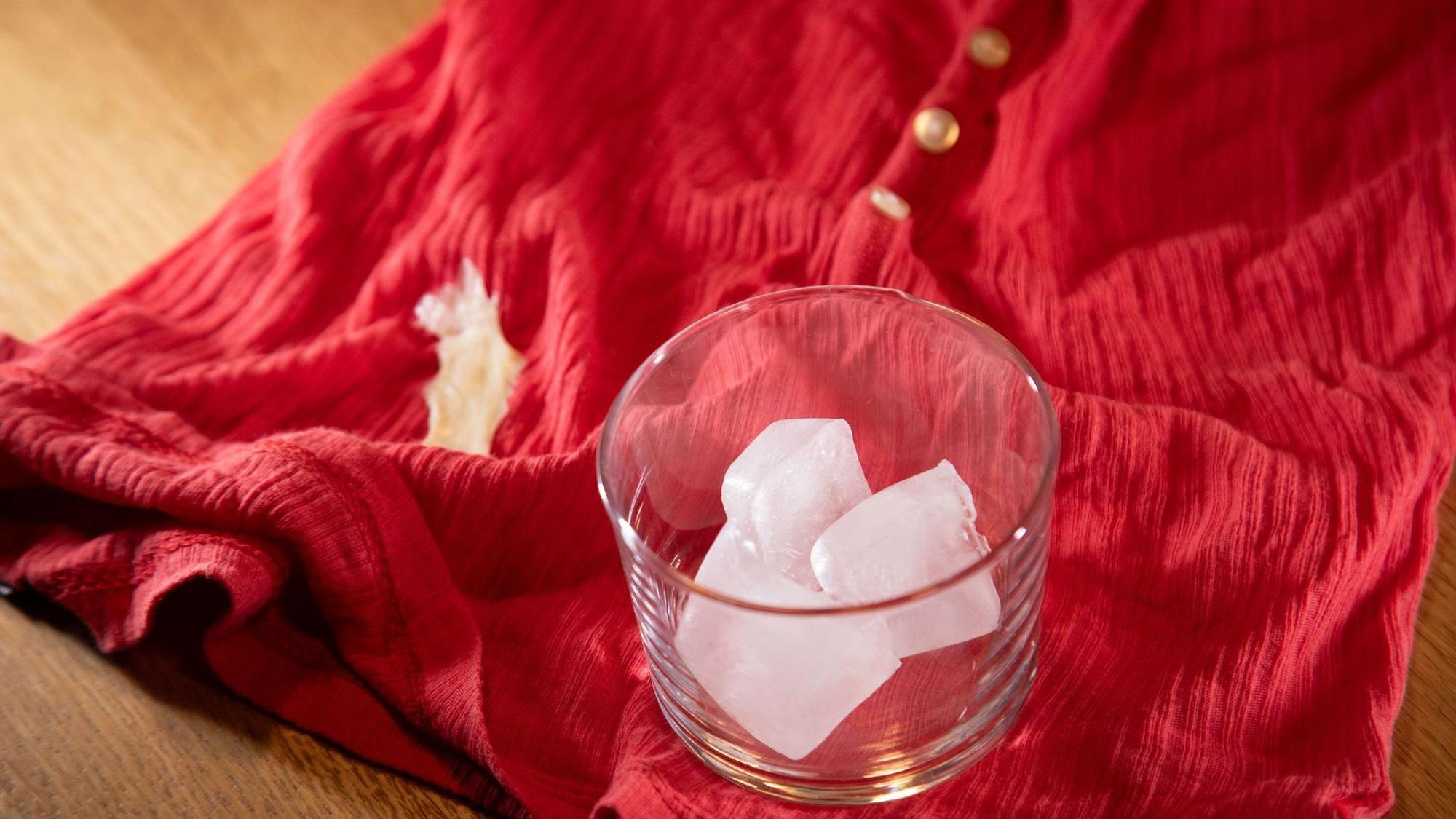 Glas mit Eiswürfeln steht auf einem Shirt mit Kaugummi-Fleck