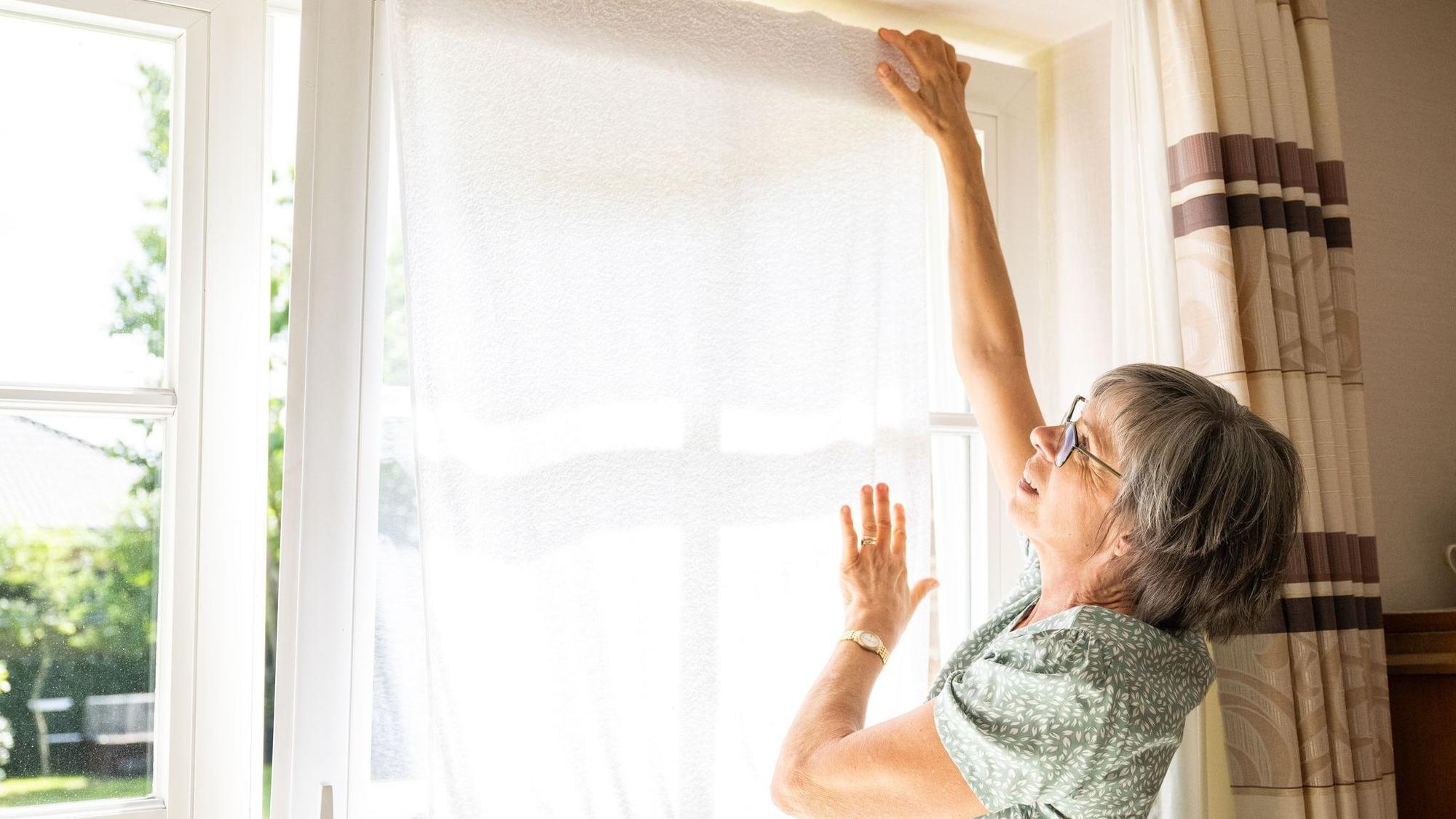 Eine Frau hängt ein nasses Handtuch vor ein Fenster
