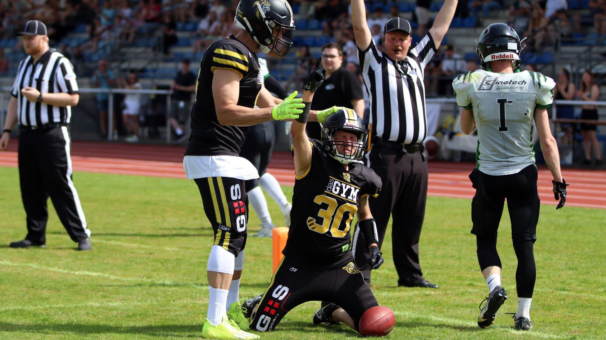 Ein Footballer jubelt über einen Touchdown, ein Mitspieler legt ihm die Hand auf den Helm.