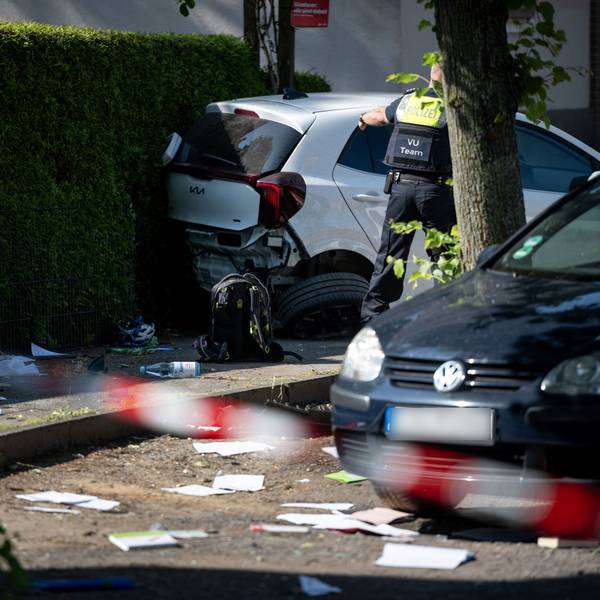 Ein Schulrucksack liegt auf dem Boden vor beschädigten Autos. Die Polizei sichert eine Unfallstelle, nachdem eine Autofahrerin drei Kinder vor einer Schule in Dinslaken verletzt hat.