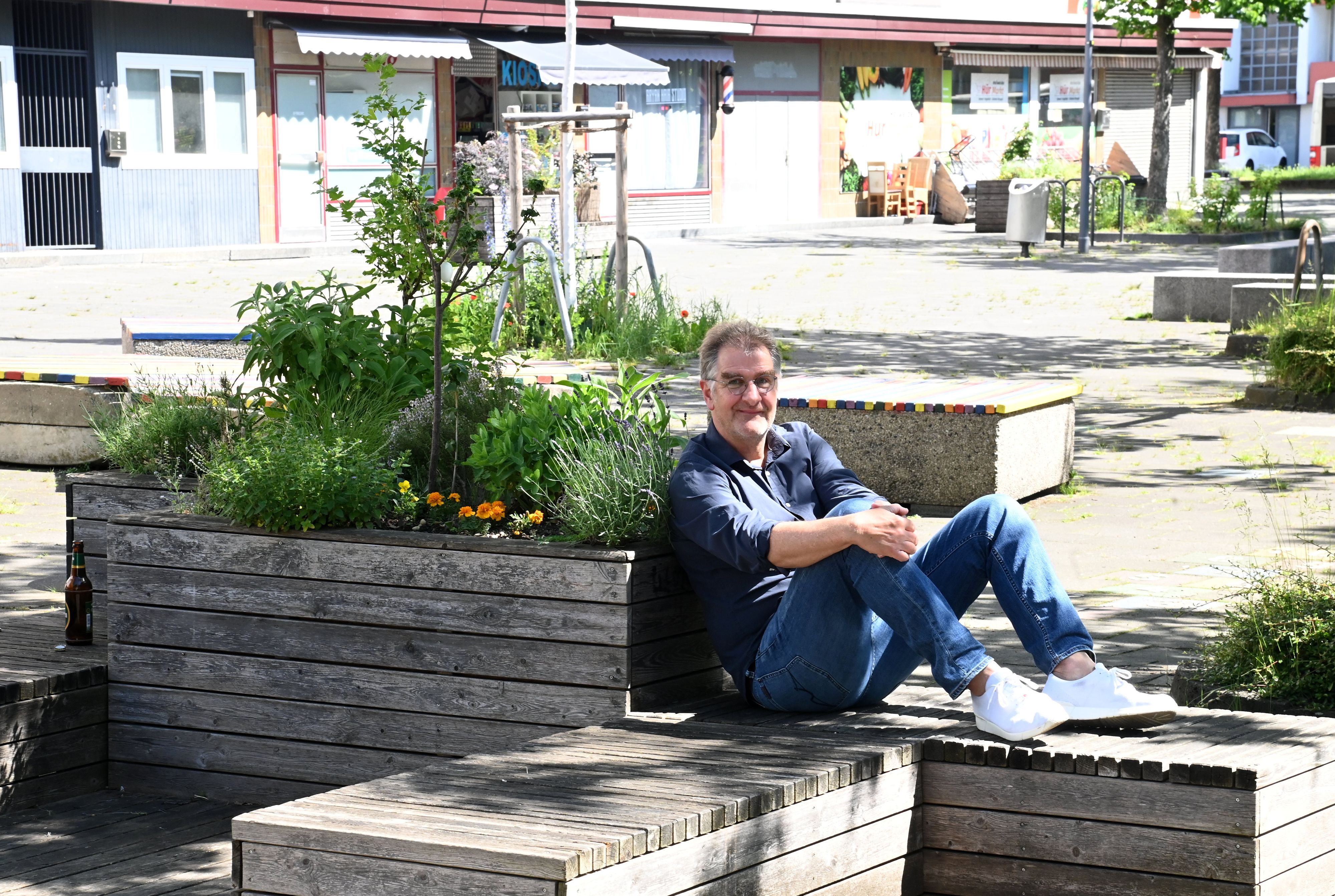Ein Mann im blauen Hemd sitzt auf einer Holzbank, mit dem Rücken an ein Holz-Hochbeet gelehnt.