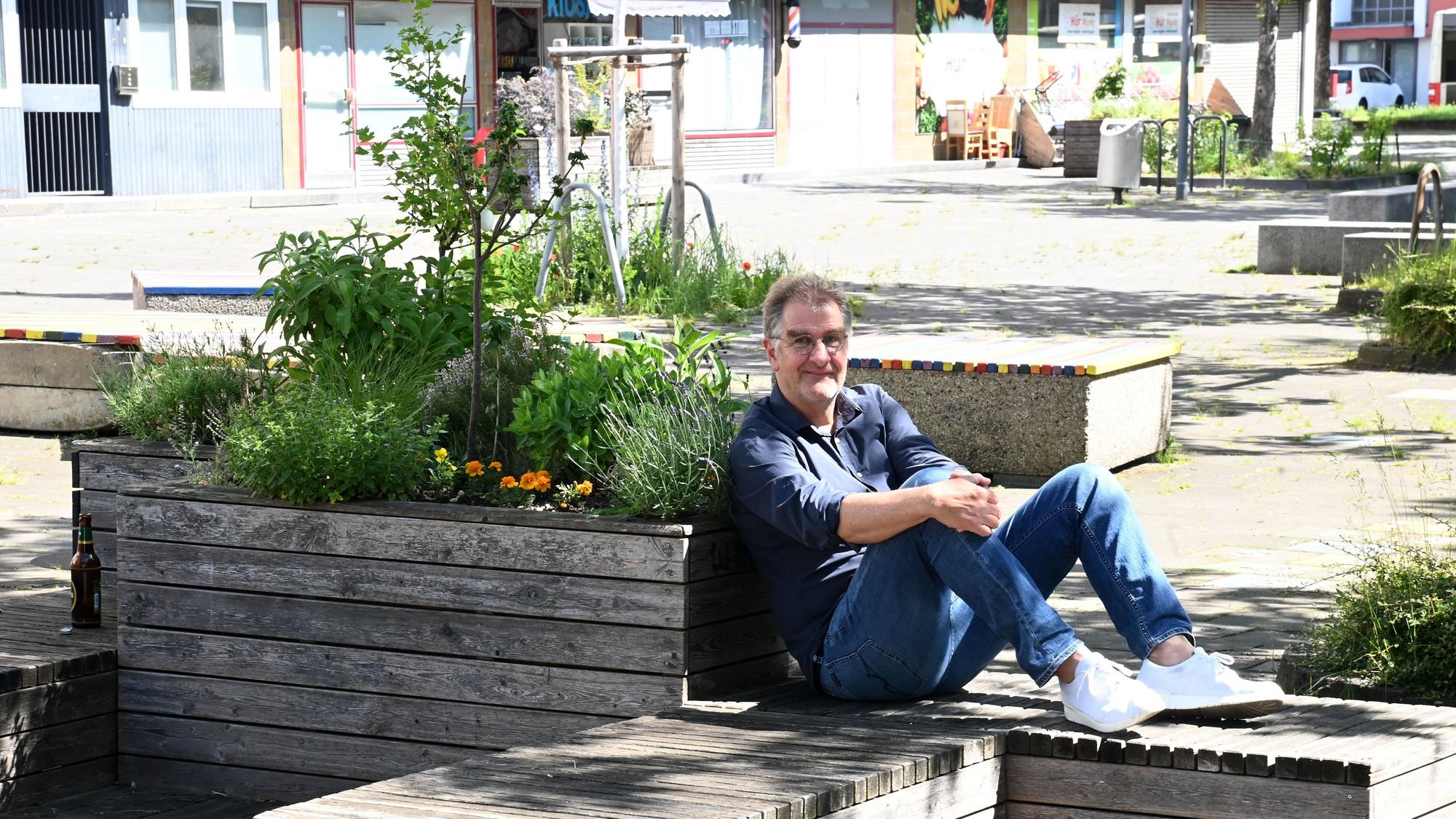 Ein Mann im blauen Hemd sitzt auf einer Holzbank, mit dem Rücken an ein Holz-Hochbeet gelehnt.