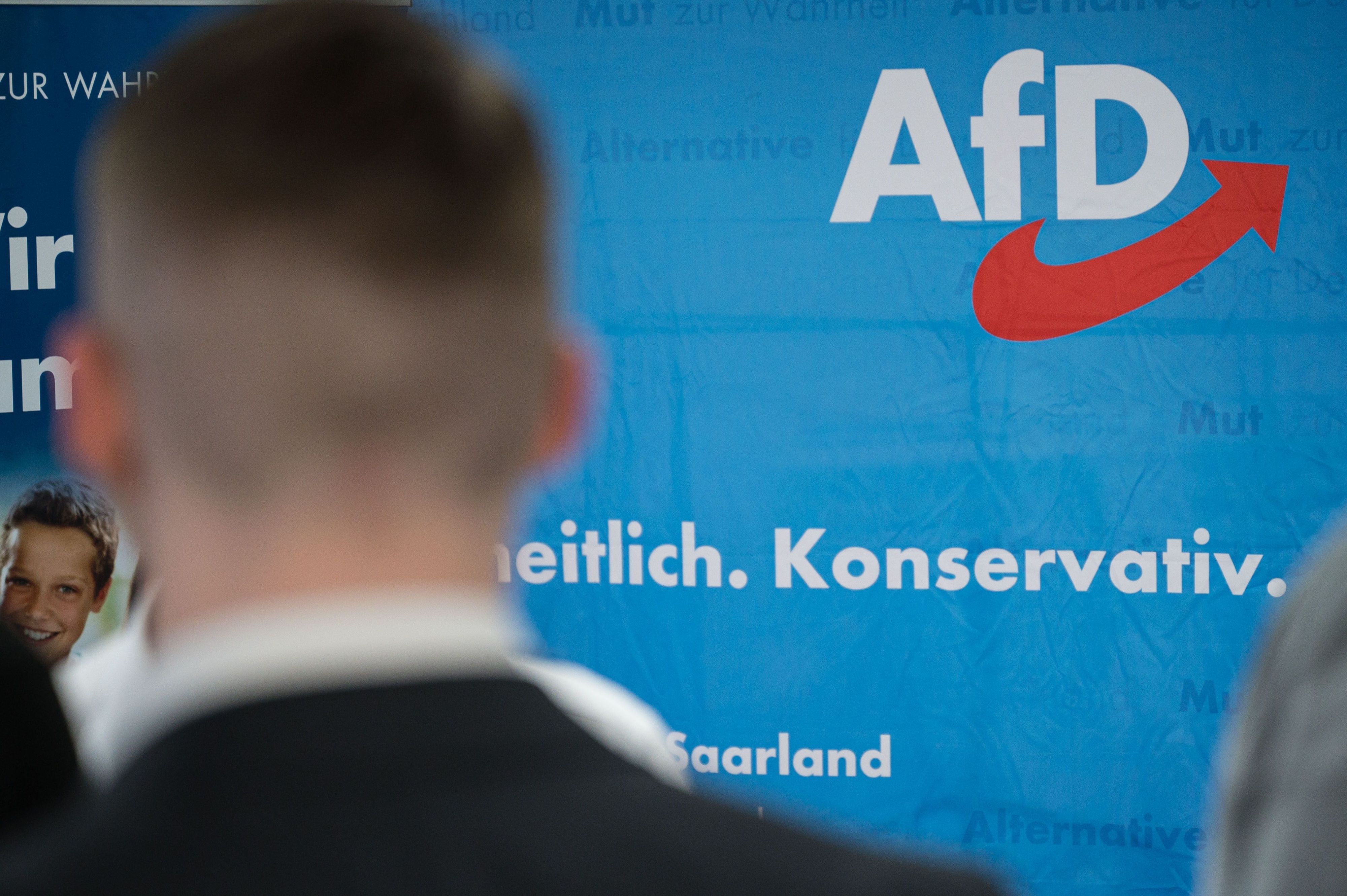 Ein Anhänger der AfD im Saarland steht auf einer Wahlparty vor einem Aufsteller der Partei.