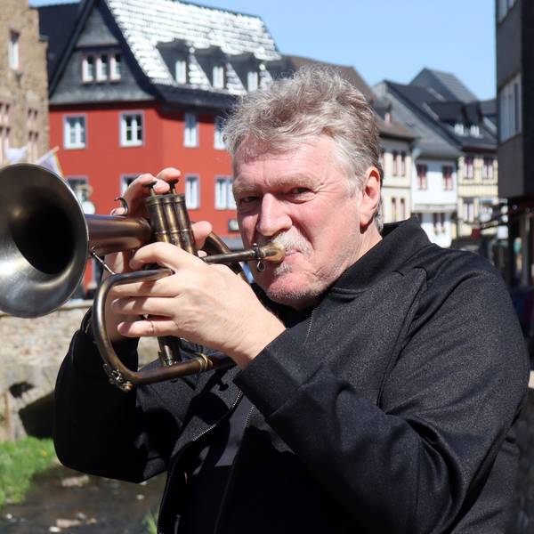 Hans Peter Salentin bläst in eine Trompete, im Hintergrund ist die Bad Münstereifeler Innenstadt zu sehen.