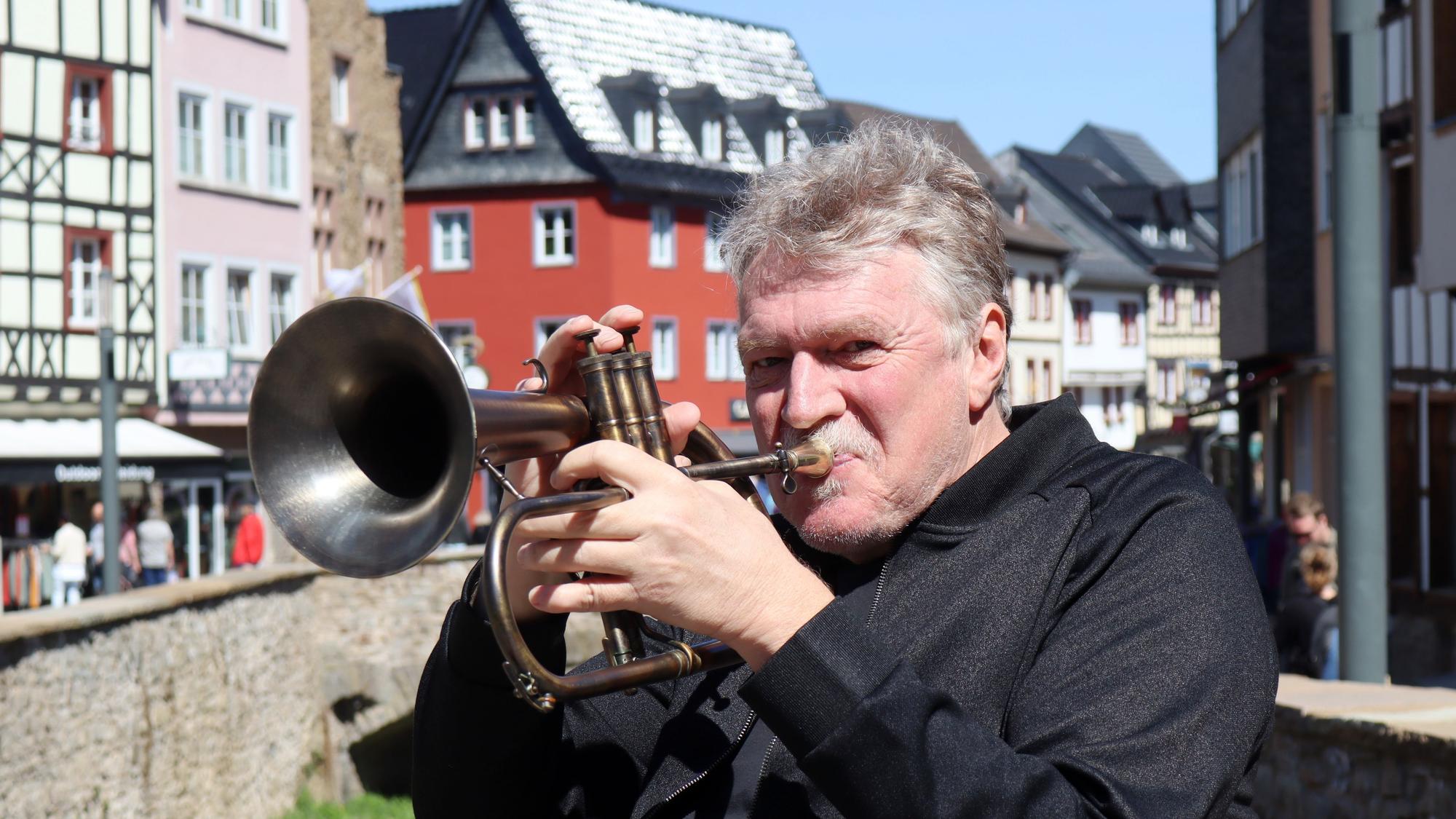 Hans Peter Salentin bläst in eine Trompete, im Hintergrund ist die Bad Münstereifeler Innenstadt zu sehen.