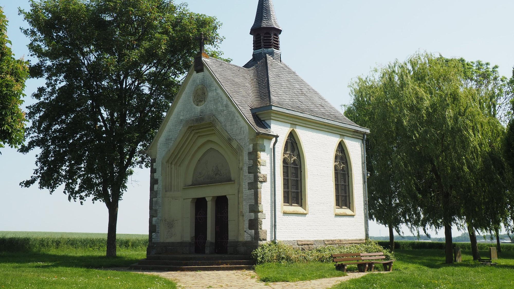Die Kapelle steht zwischen Bäumen, ein Kiesweg führt zum Eingang.