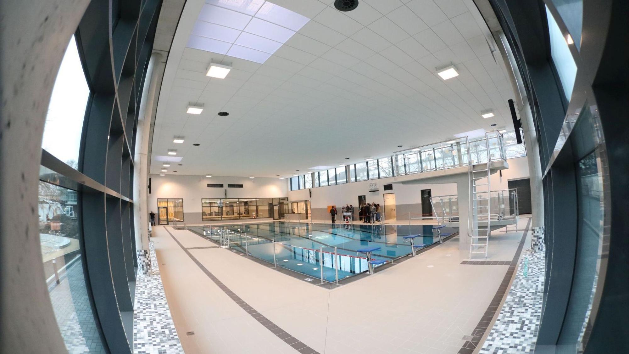 Blick in ein Hallenbad, am rechten Rand steht ein Drei-Meter-Sprungturm.