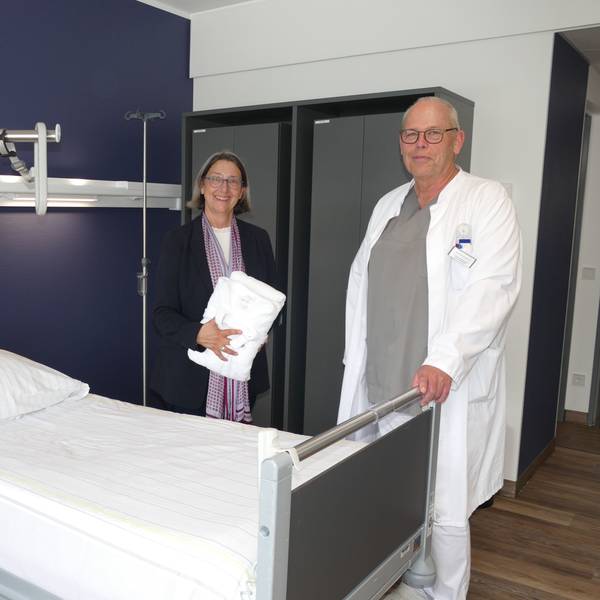 Ein Arzt und eine Frau in Zivilkleidung an einem Krankenbett.