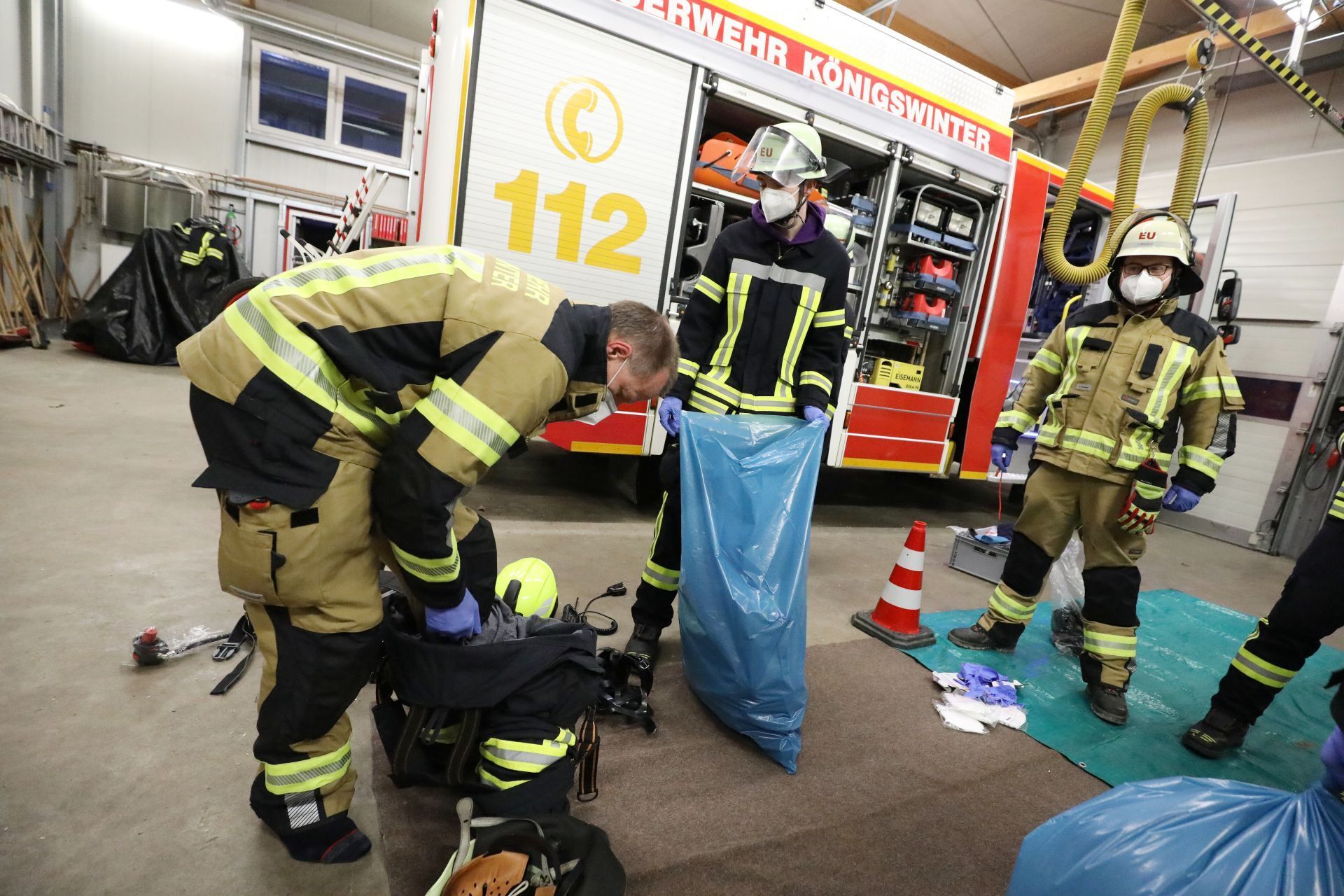 Feuerwehrleute in Schutzkleidung und mit Maske verstauen Einsatzkleidung in blauen Müllsäcken.