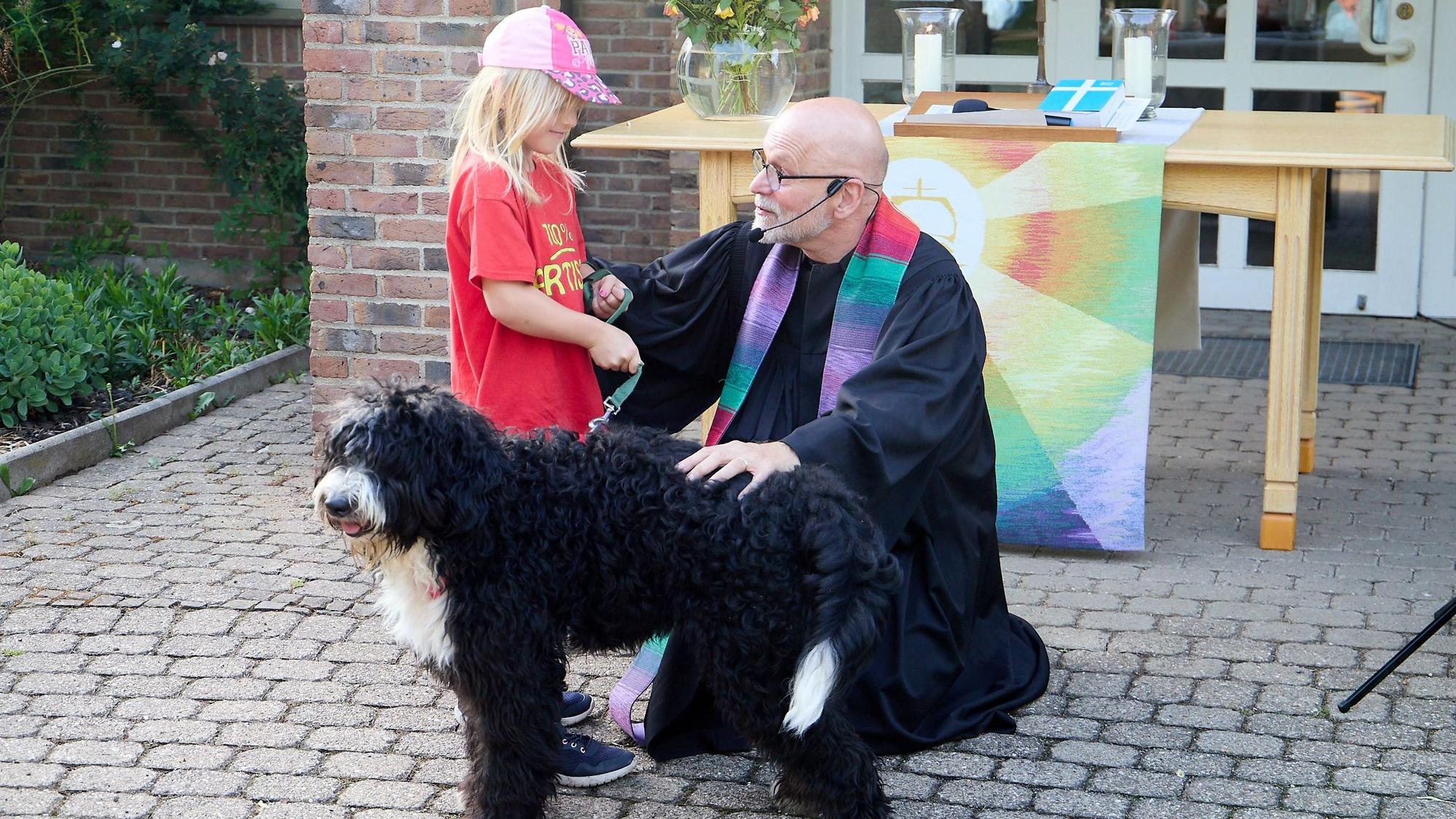Ein Kind und ein Hund stehen neben einem knieenden Geistlichen.