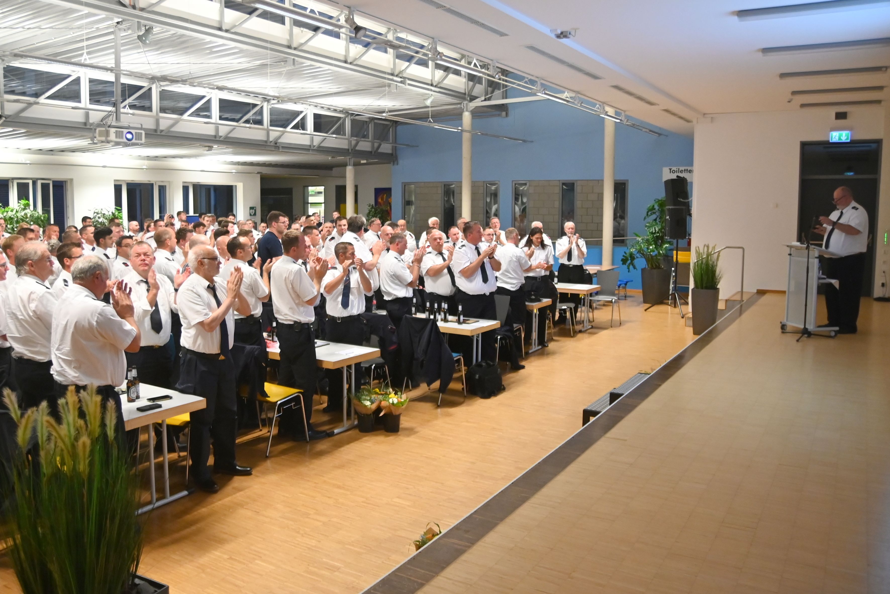 Ein Saal voller Feuerwehrleute applaudiert einem Mann auf der Bühne.