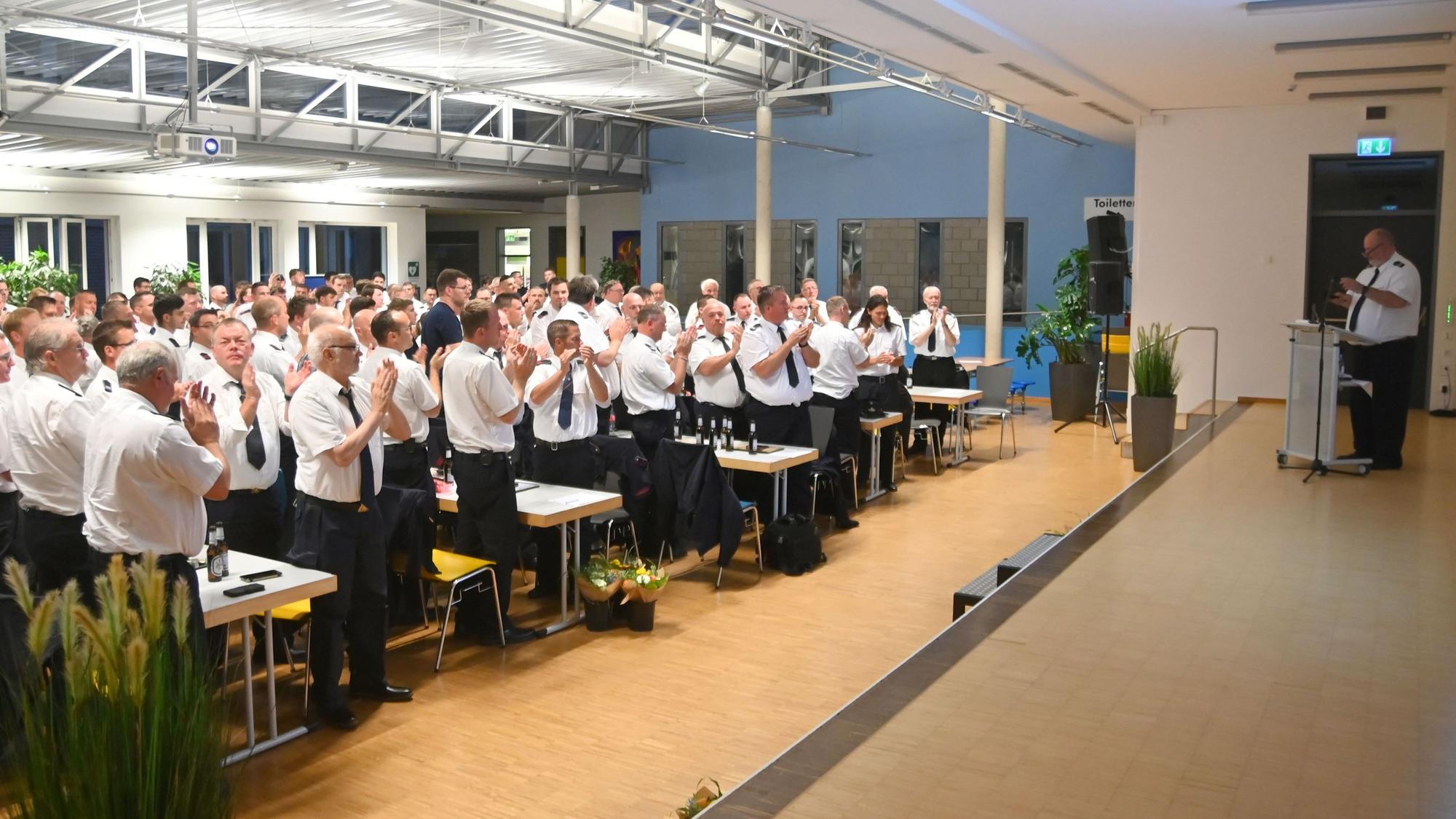 Ein Saal voller Feuerwehrleute applaudiert einem Mann auf der Bühne.