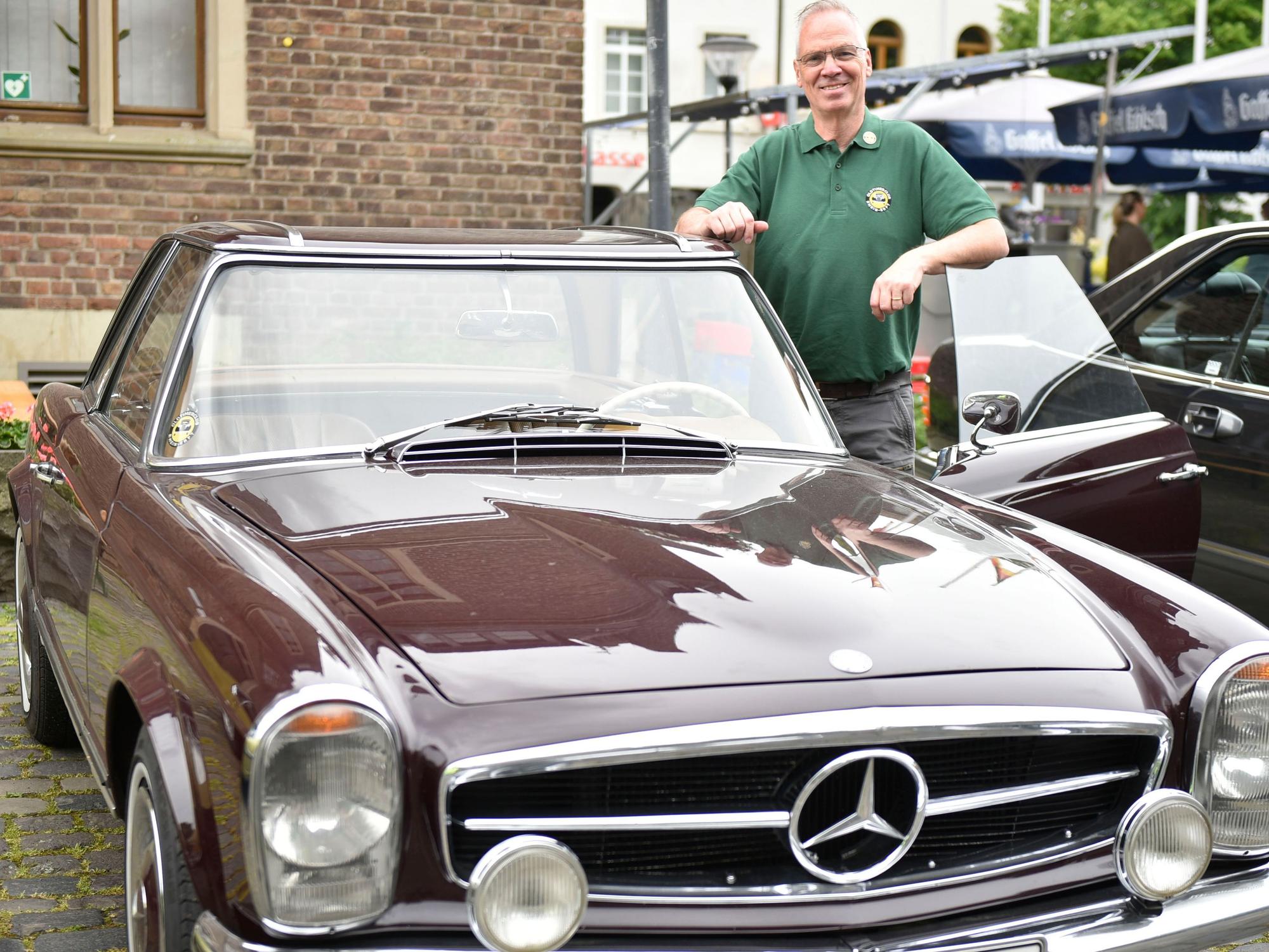 Ein Mann steht in der geöffneten Tür seiens dunkelroten Mercedes 250 SC von 1967.
