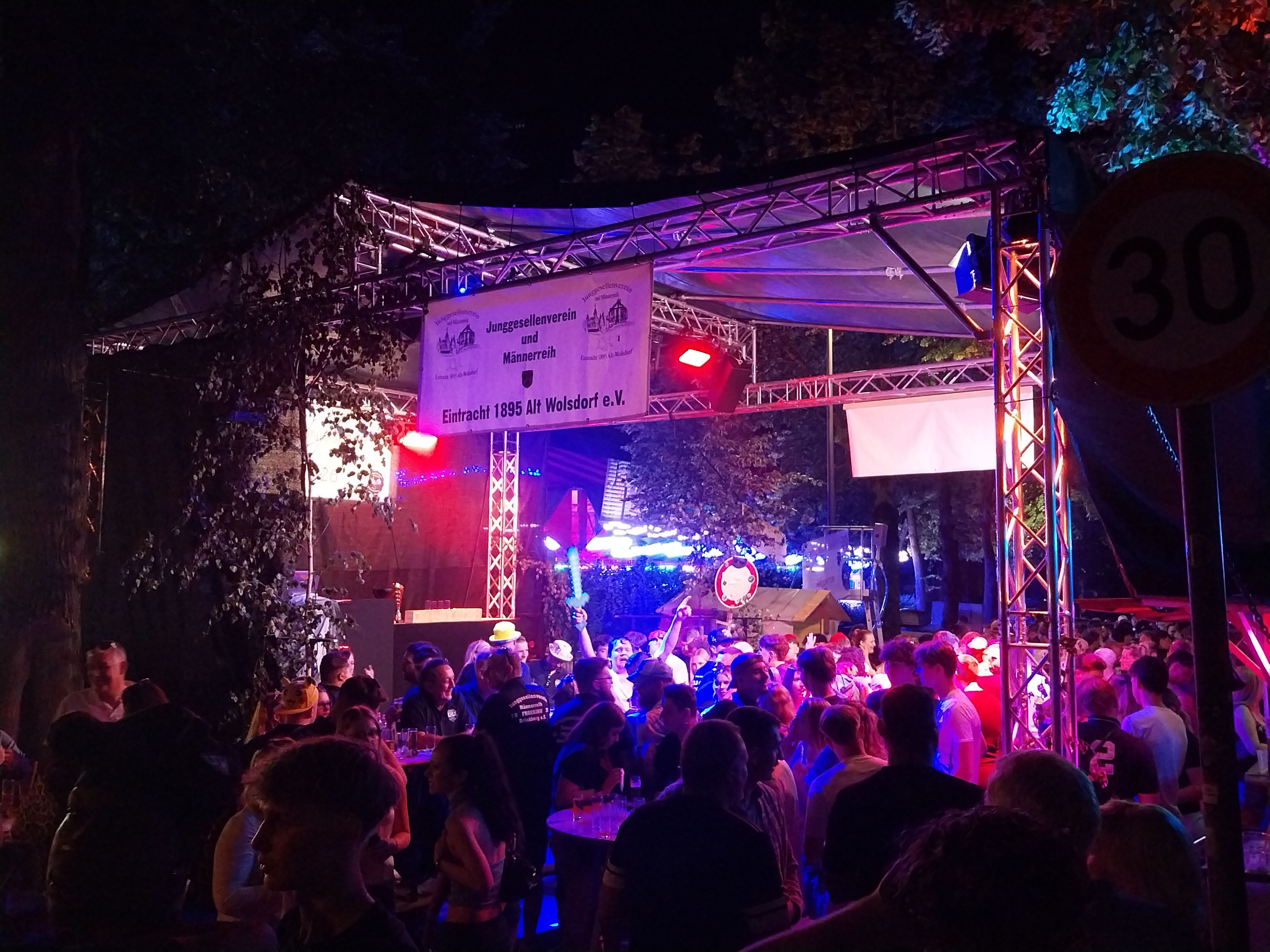 Eine Menschenmenge feiert im Partylicht vor einer Bühne.
