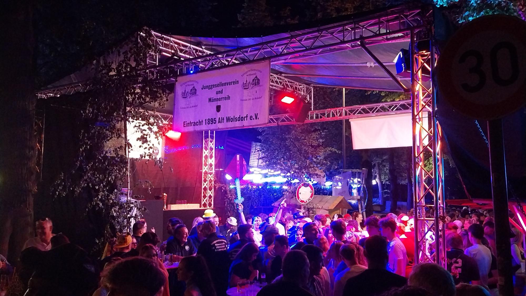 Eine Menschenmenge feiert im Partylicht vor einer Bühne.