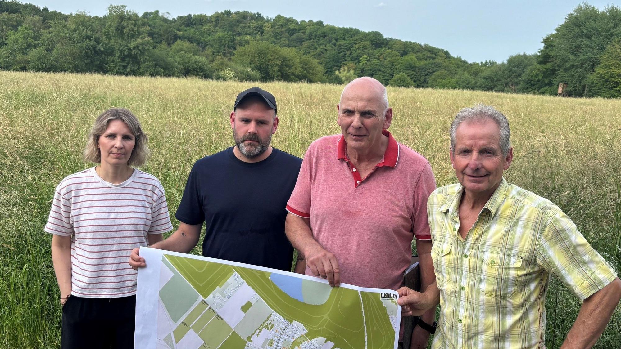 Auf dem Bild ist eine Gruppe von drei Männern und einer Frau zu sehen, die vor einem Feld stehen. Sie halten einen Plan in der Hand.