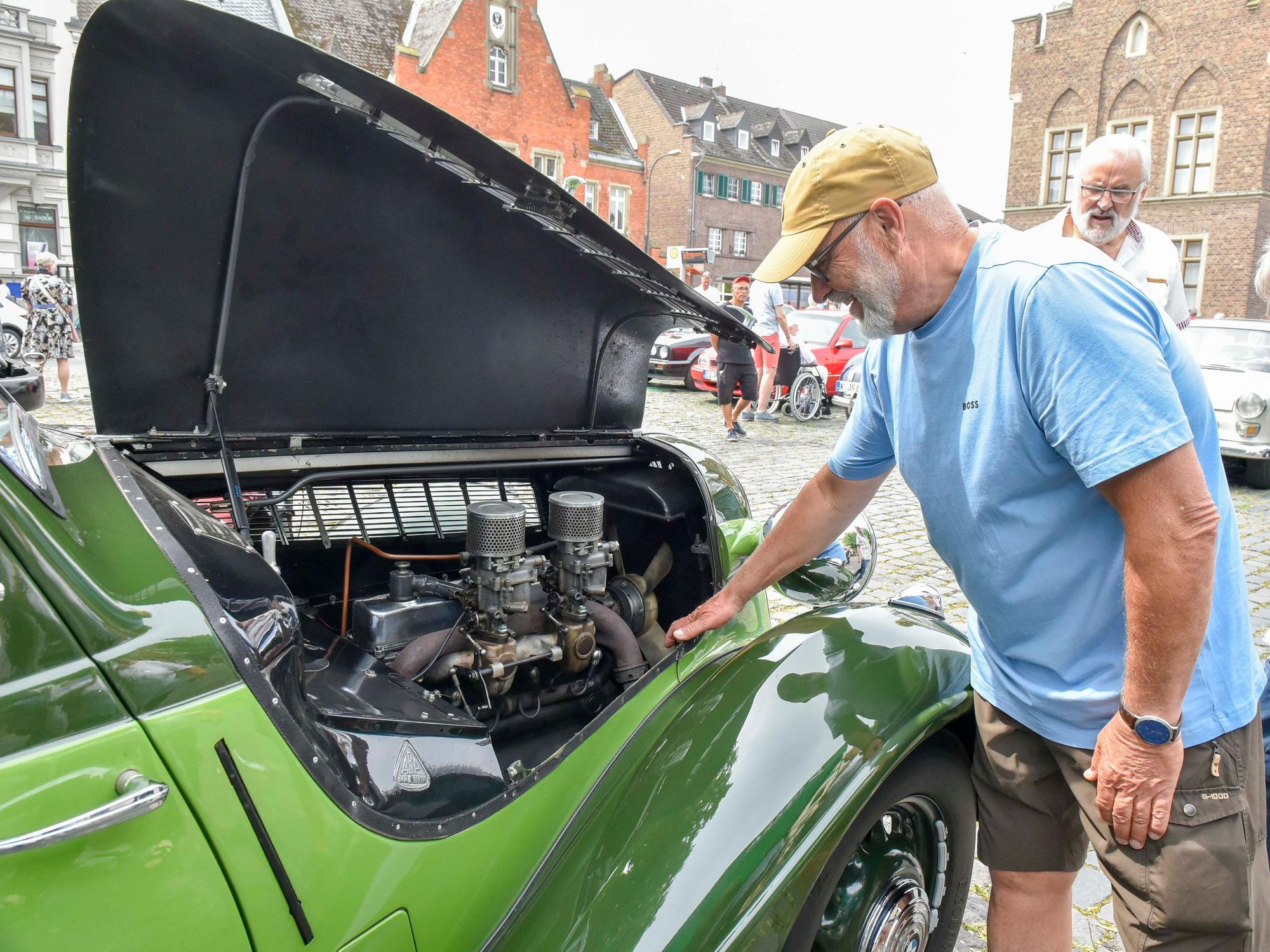 Ein Mann schaut in die Motorhaube eines Oldtimers.
