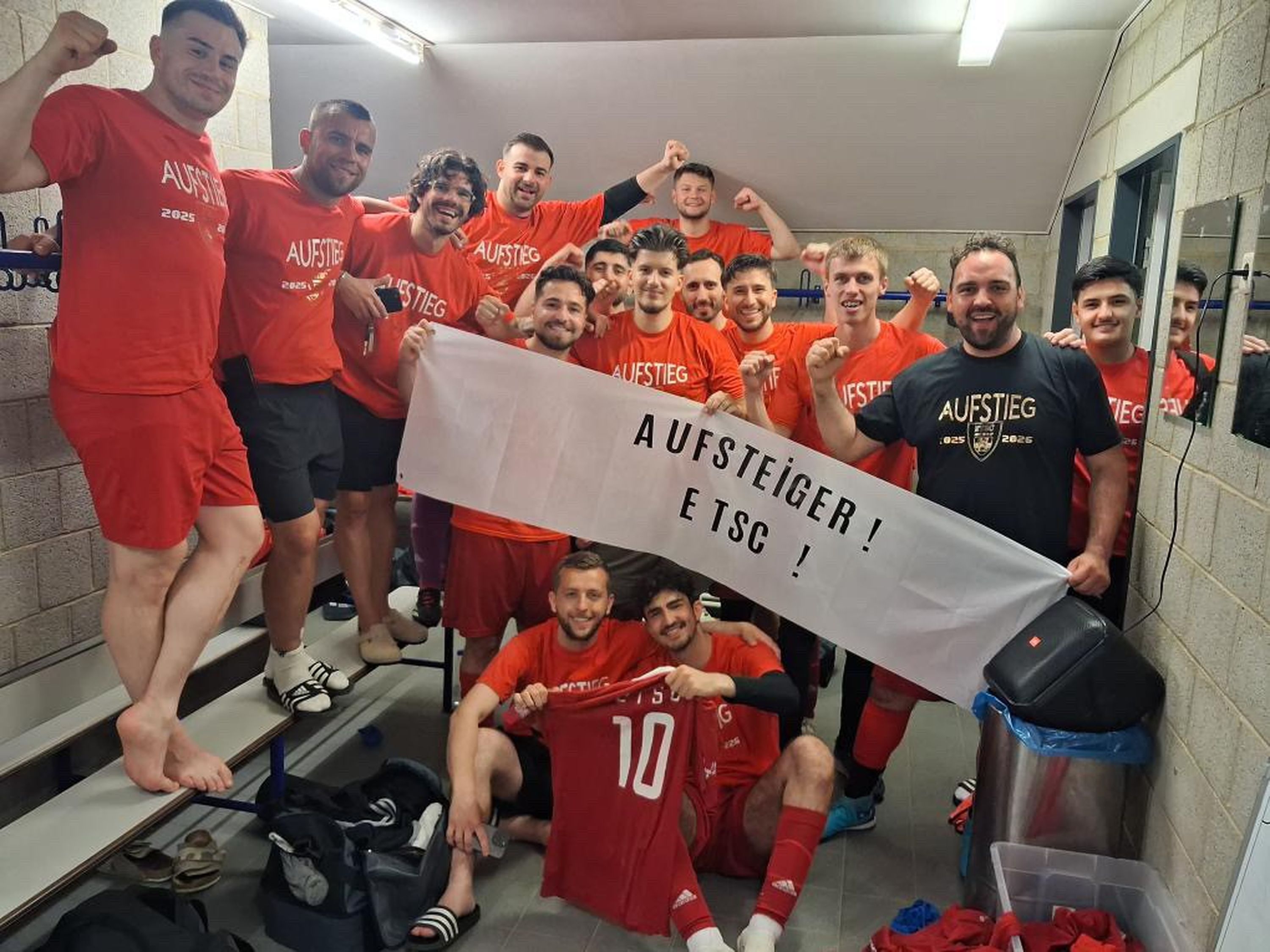 Die Mannschaft des Euskirchener TSC freut sich in der Kabine über den Aufstieg. Die Spieler halten ein Transparent mit der Aufschrift "Aufsteiger! ETSC!" hoch.