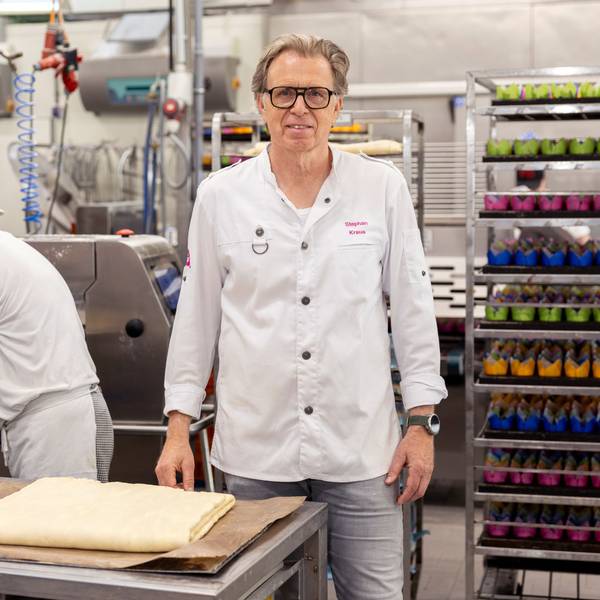 Stephan Kraus steht in der Produktionshalle der Bäckerei Kraus. Hinter ihm hievt ein Mitarbeiter Teig auf ein Band.