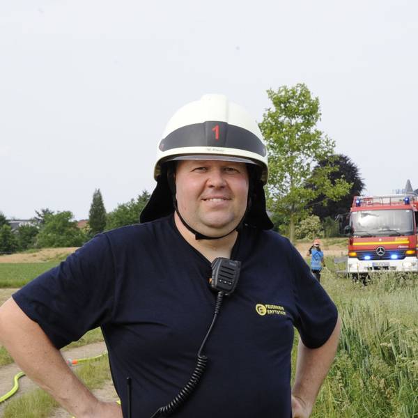 Ein Mann in Feuerwehrhelm steht vor einem Einsatzfahrzeug.