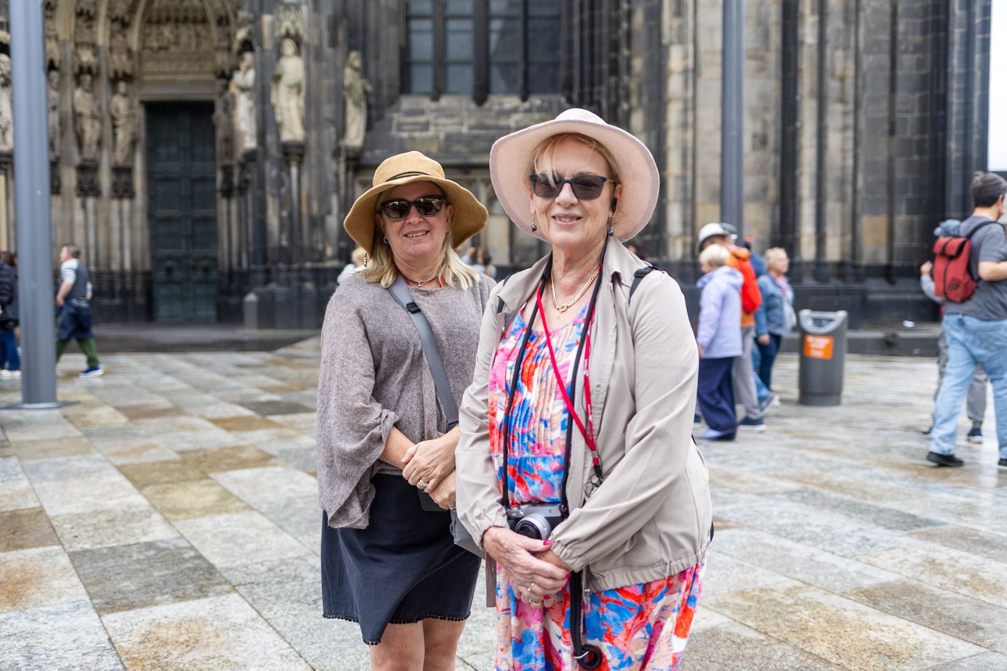 Zwei Frauen mit Sonnenhut und Brille stehen vor dem Dom.