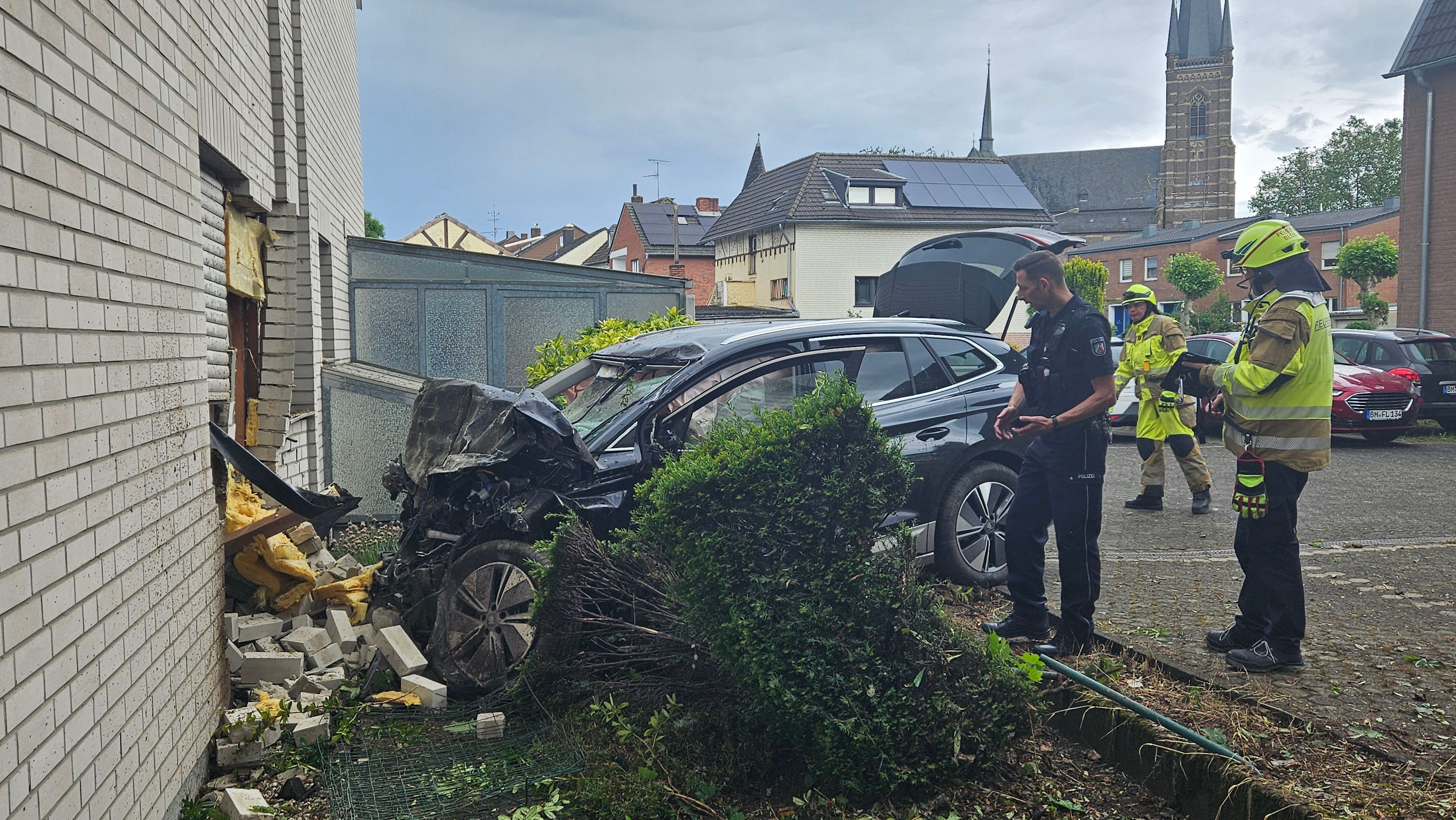 Das Bild zeigt ein Auto an einer Hauswand und Einsatzkräfte.