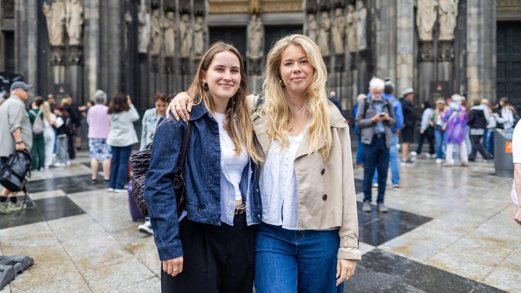 Zwei Frauen stehen Arm in Arm vor einer Menschenmasse am Dom
