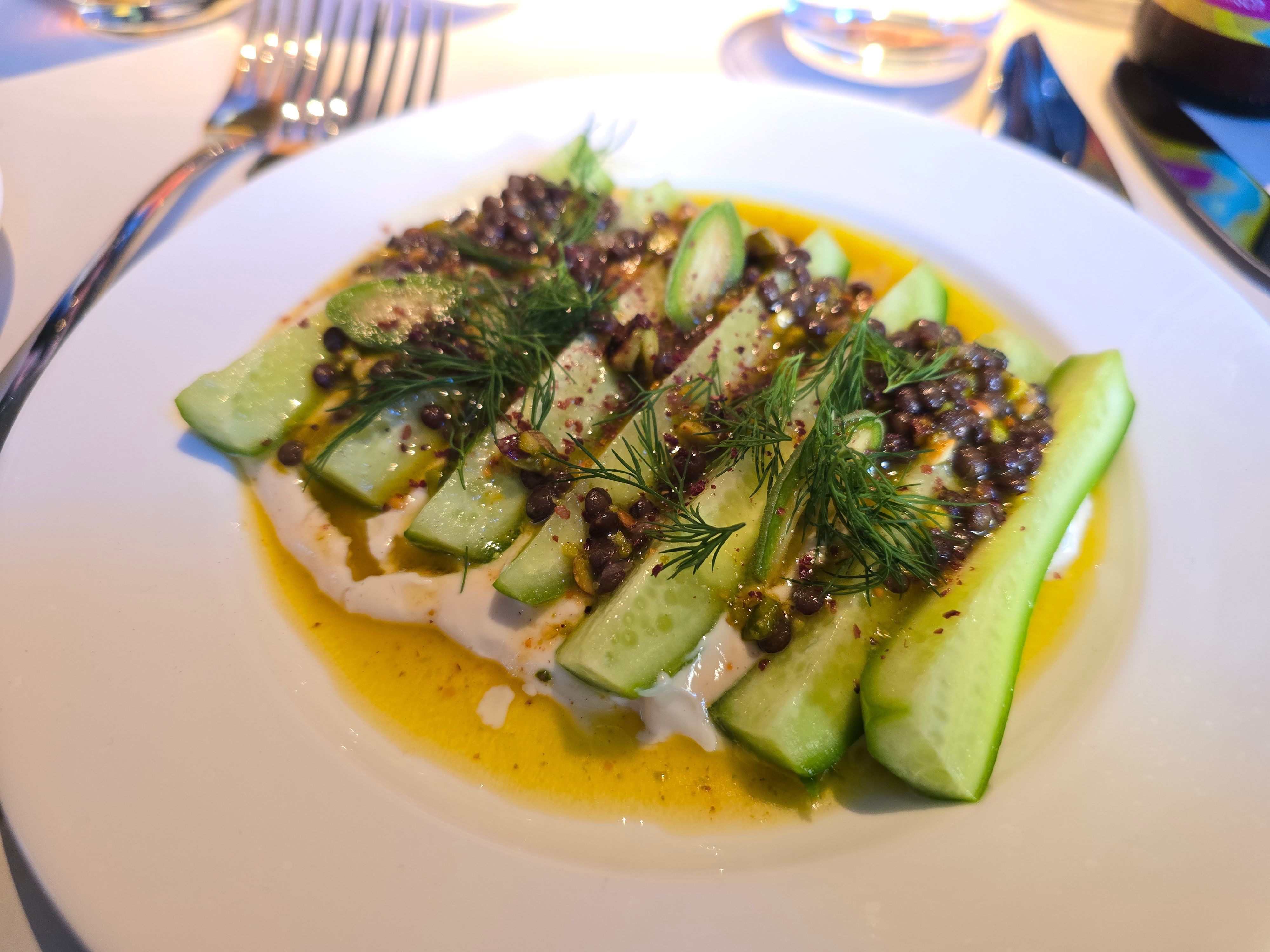 Geviertelte, rohe Minigurken auf einem cremigen Mandel-Tahini-Bett, on top Beluga-Linsen, crunchy Pistazien und Dill