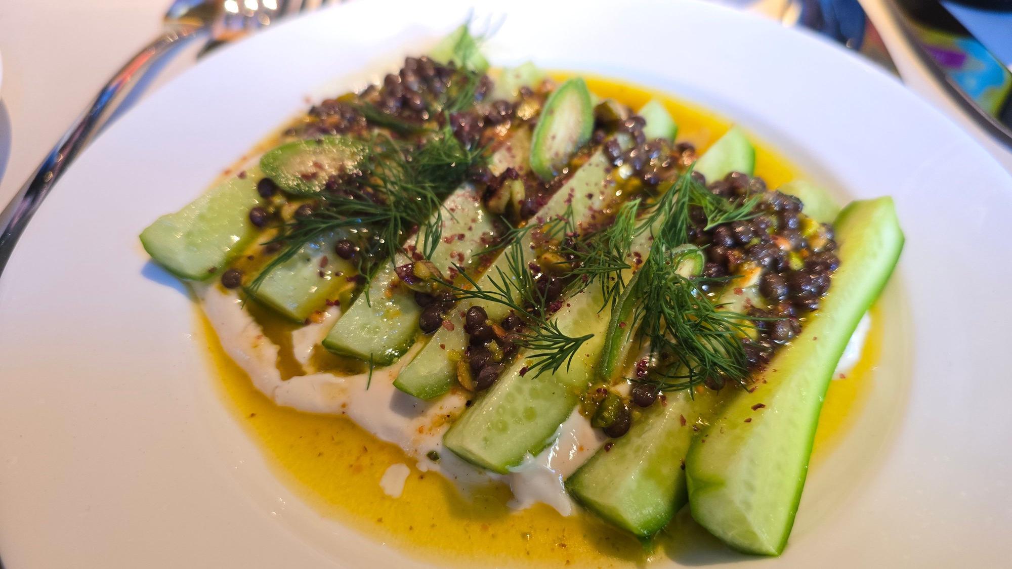 Geviertelte, rohe Minigurken auf einem cremigen Mandel-Tahini-Bett, on top Beluga-Linsen, crunchy Pistazien und Dill