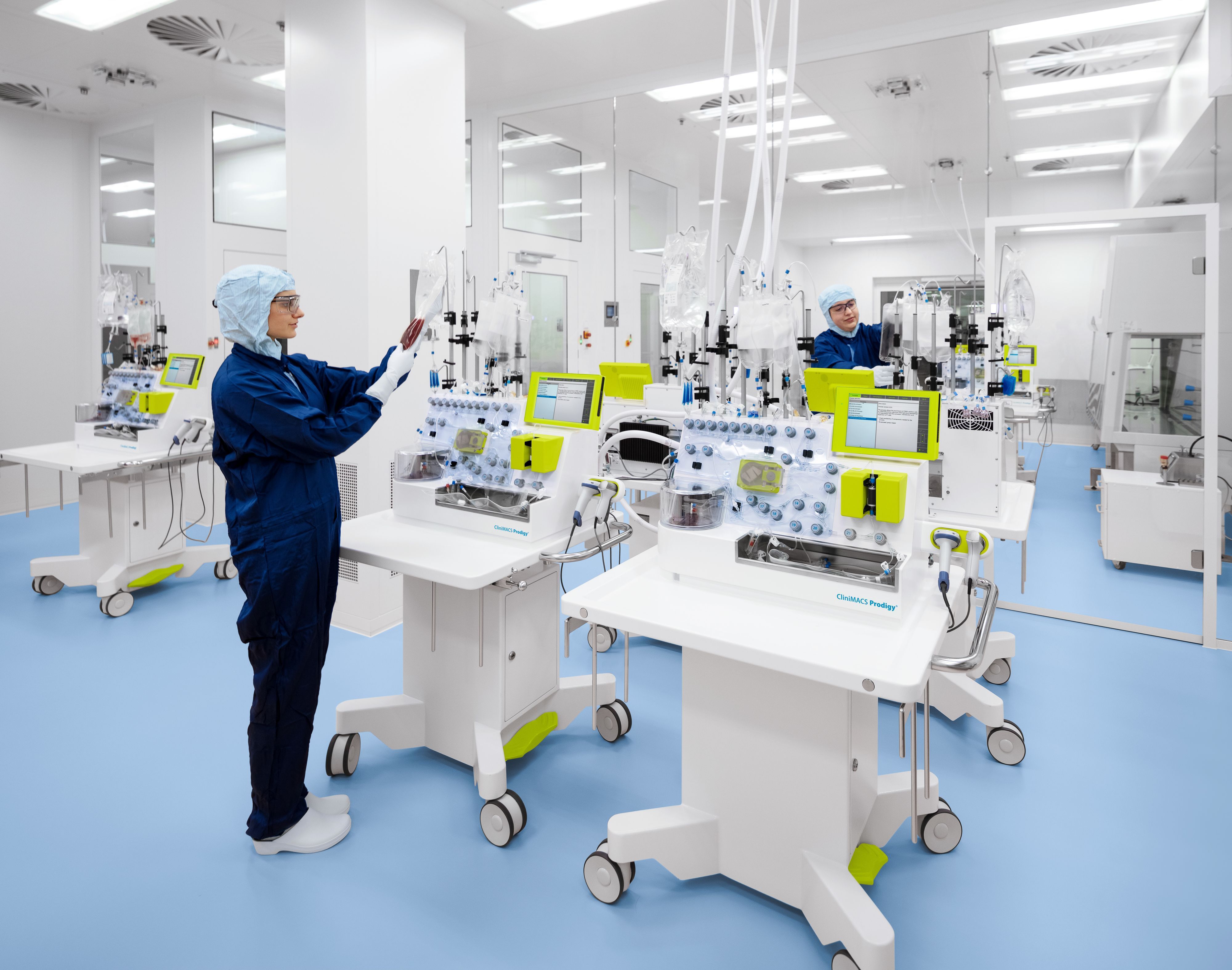 Eine Mitarbeiterin in einem blauen Overall arbeitet an weißen Laborgeräten in einem Reinraum.