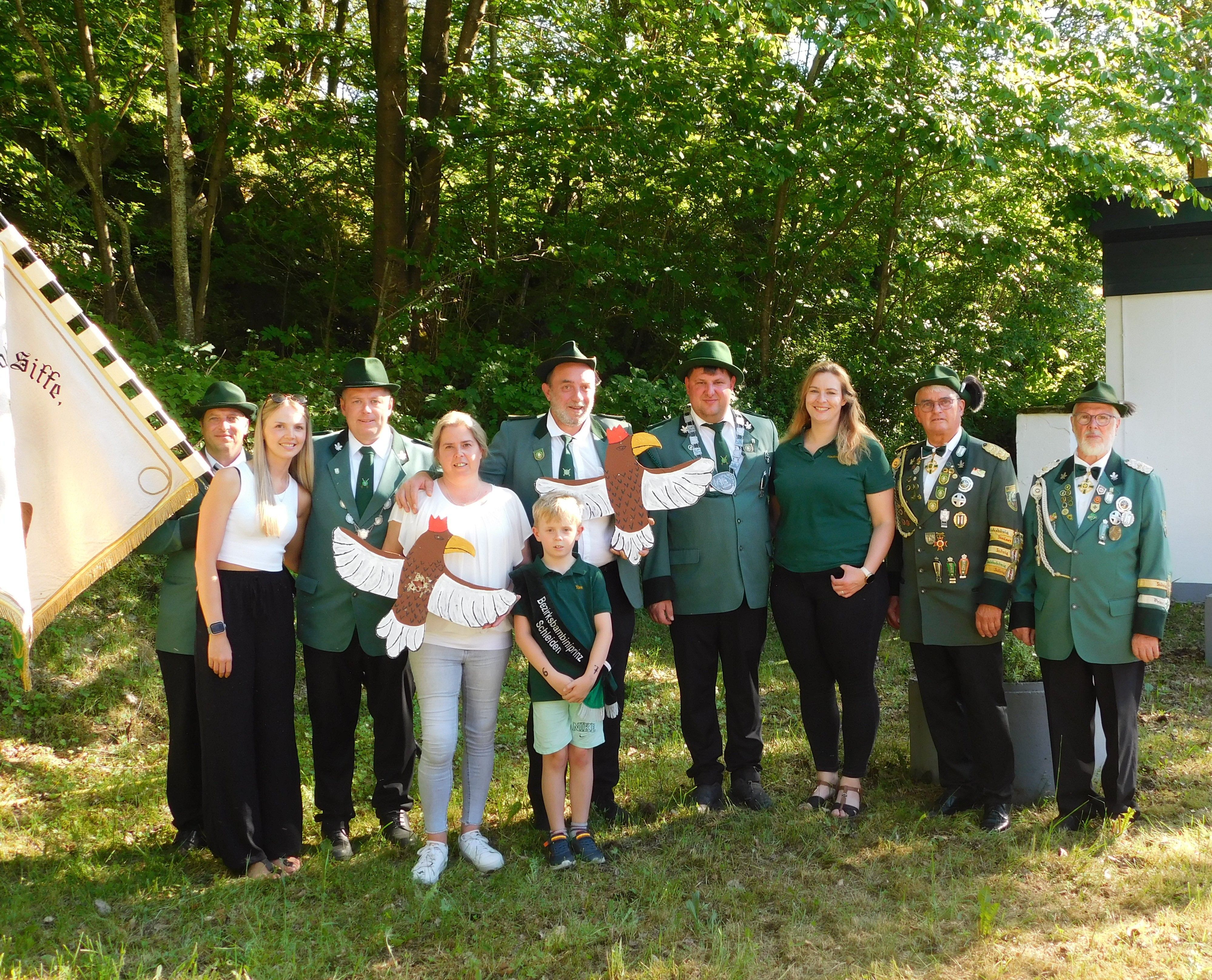 Eine Gruppe Menschen steht in Schützenuniform nebeneinander auf einer Wiese vor Bäumen.