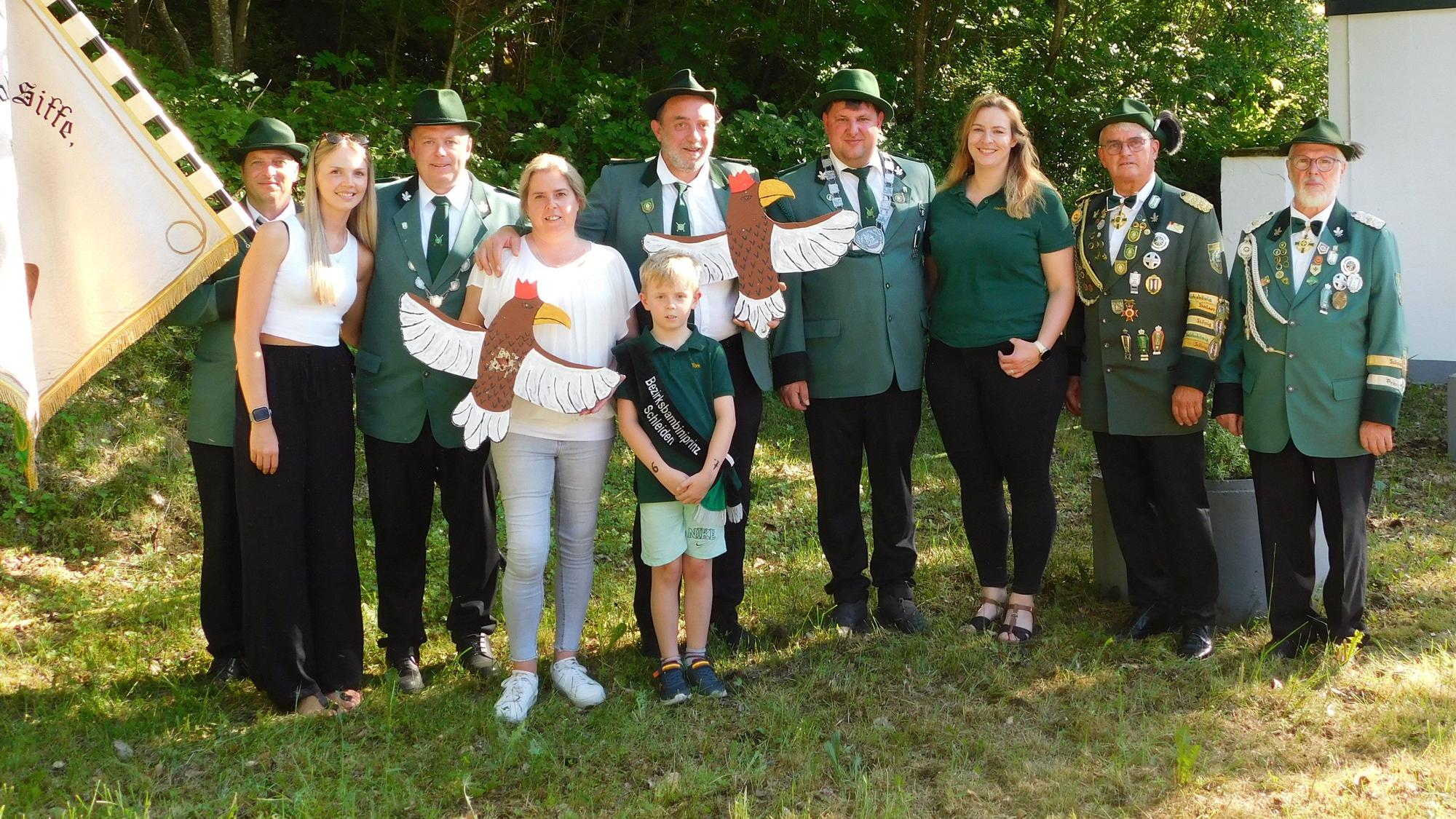 Eine Gruppe Menschen steht in Schützenuniform nebeneinander auf einer Wiese vor Bäumen.