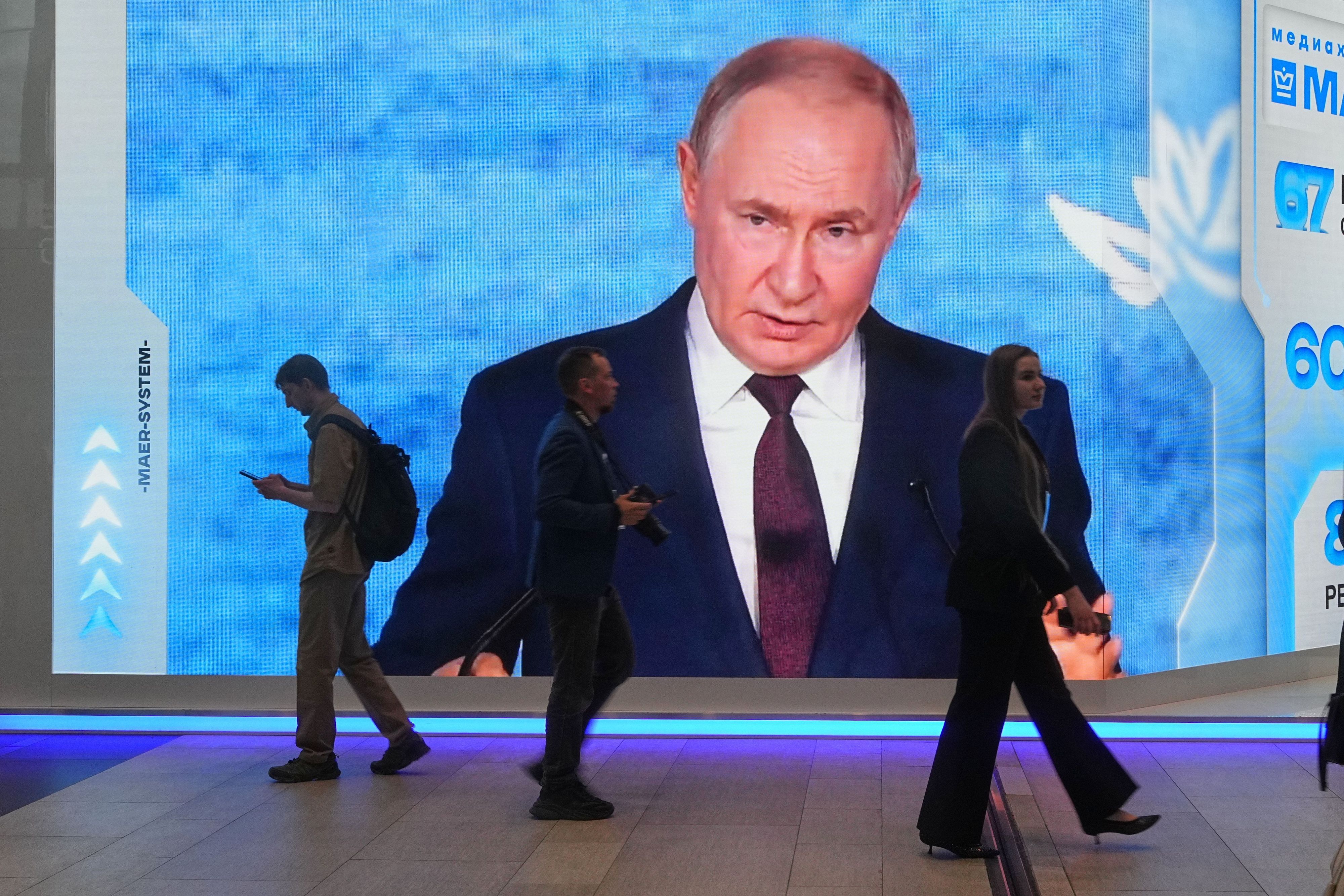 Menschen gehen an einem Bildschirm mit einem Bild des russischen Präsidenten Wladimir Putin auf dem Internationalen Wirtschaftsforum in St. Petersburg vorbei.