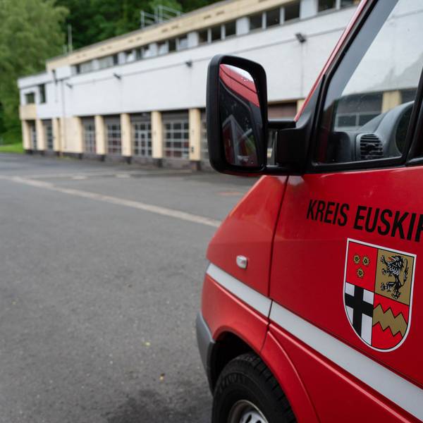 Im Hintergrund ist das Brandschutzzentrum des Kreises Euskirchen in Schleiden zu sehen, im Vordergrund ein Feuerwehrfahrzeug mit dem Kreis-Wappen und der Aufschrift „Kreis Euskirchen“.