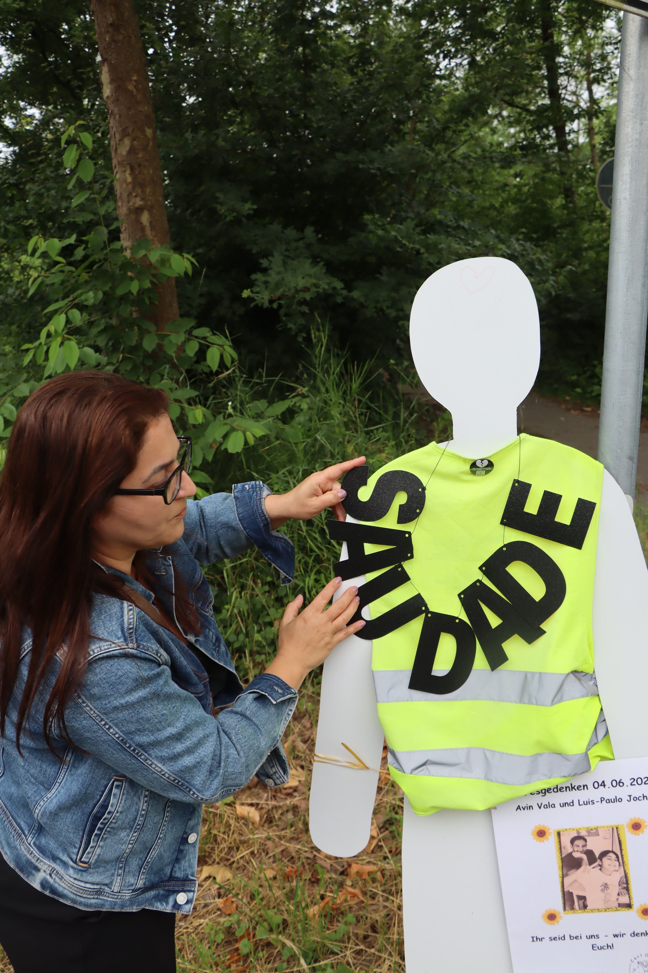 Zu sehen ist eine Frau, die zum Gedenken eine Schriftgirlande an einer Unfallstelle anbringt.