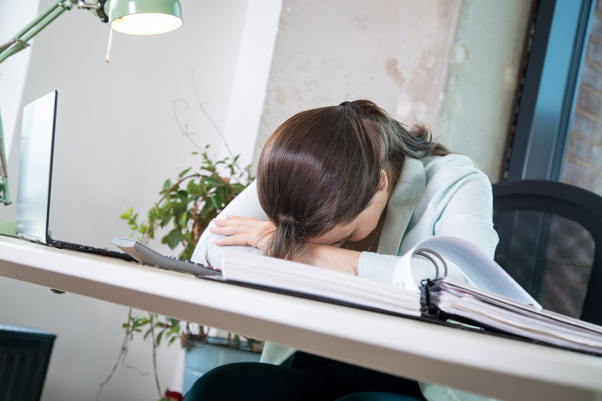Eine Frau legt ihren Kopf erschöpft auf den Schreibtisch