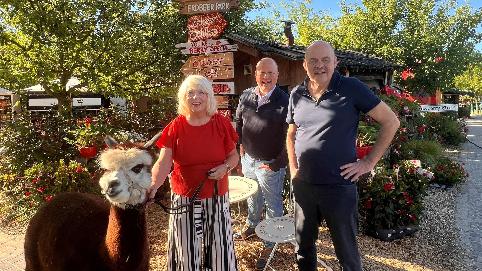Das Foto zeigt das Autorenpaar und den Landwirt mit einem Lama auf dem Gertrudenhof.