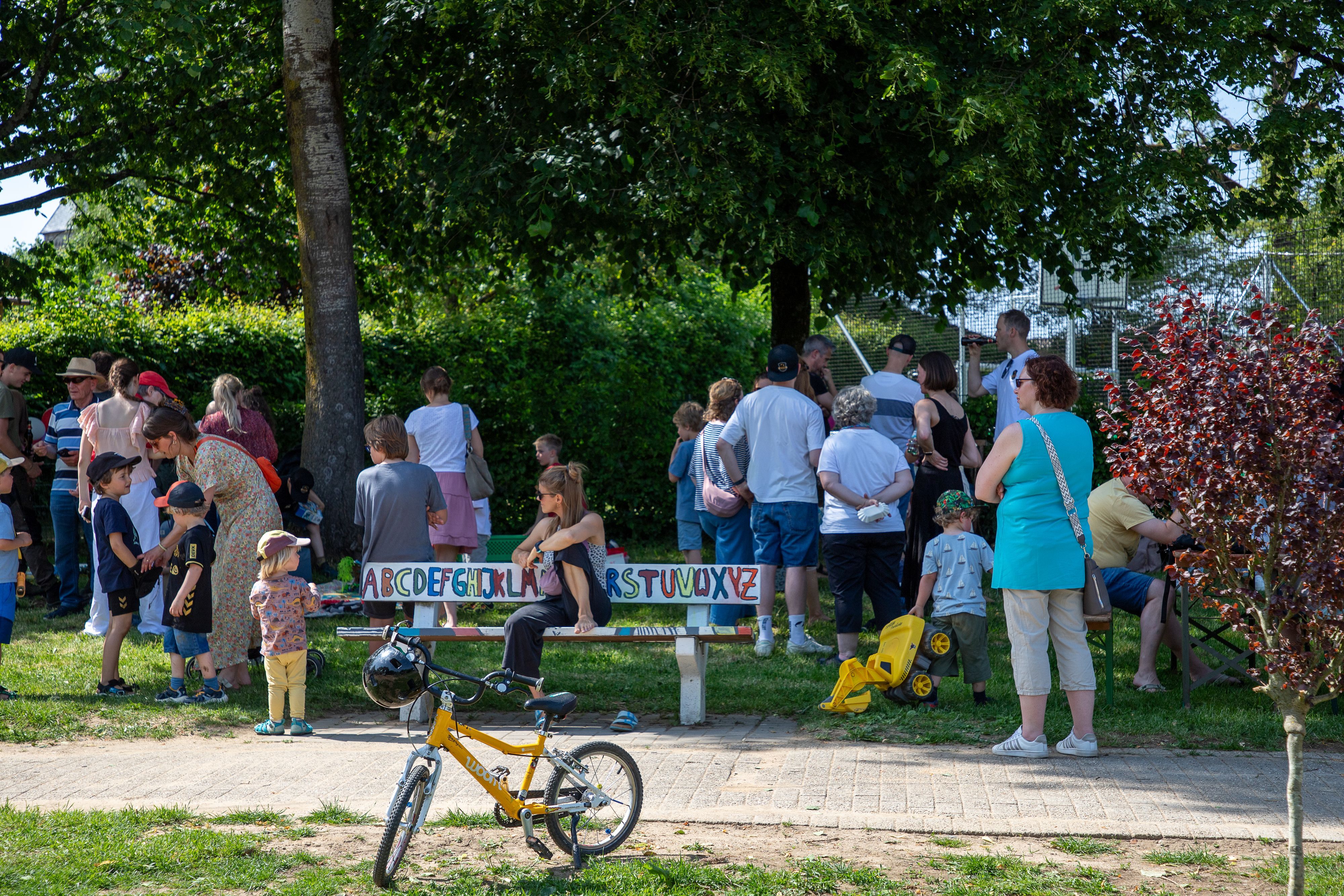 Eine gruppe Menschen steht am neuen Spielplatz in Marialinden, in Vordergrund ein gelbes Kinderfahrrad.