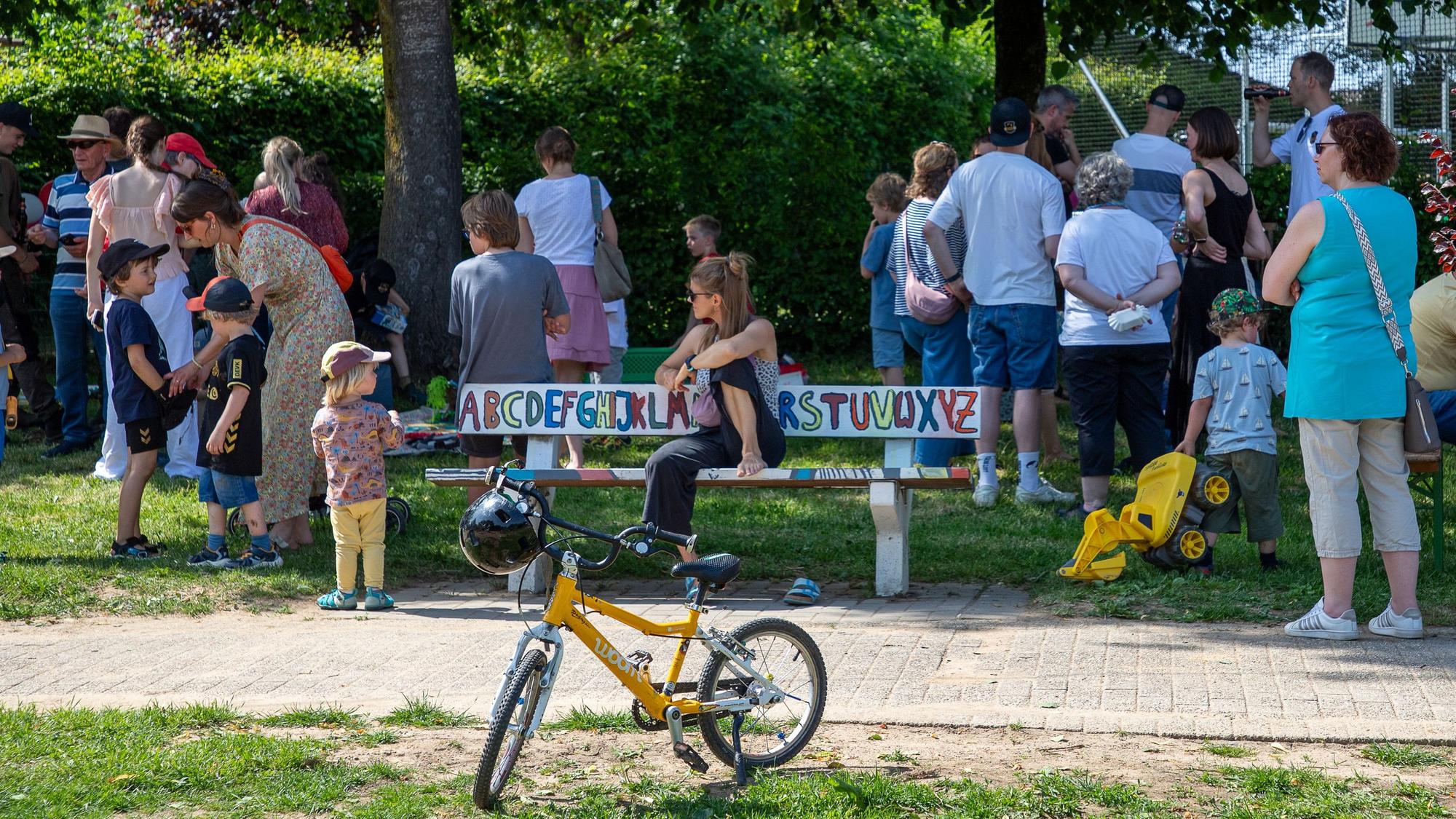 Eine gruppe Menschen steht am neuen Spielplatz in Marialinden, in Vordergrund ein gelbes Kinderfahrrad.