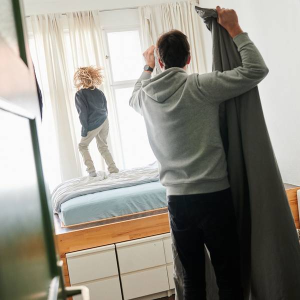 Ein Mann bezieht ein Bett während ein Kind auf dem Bett hüpft