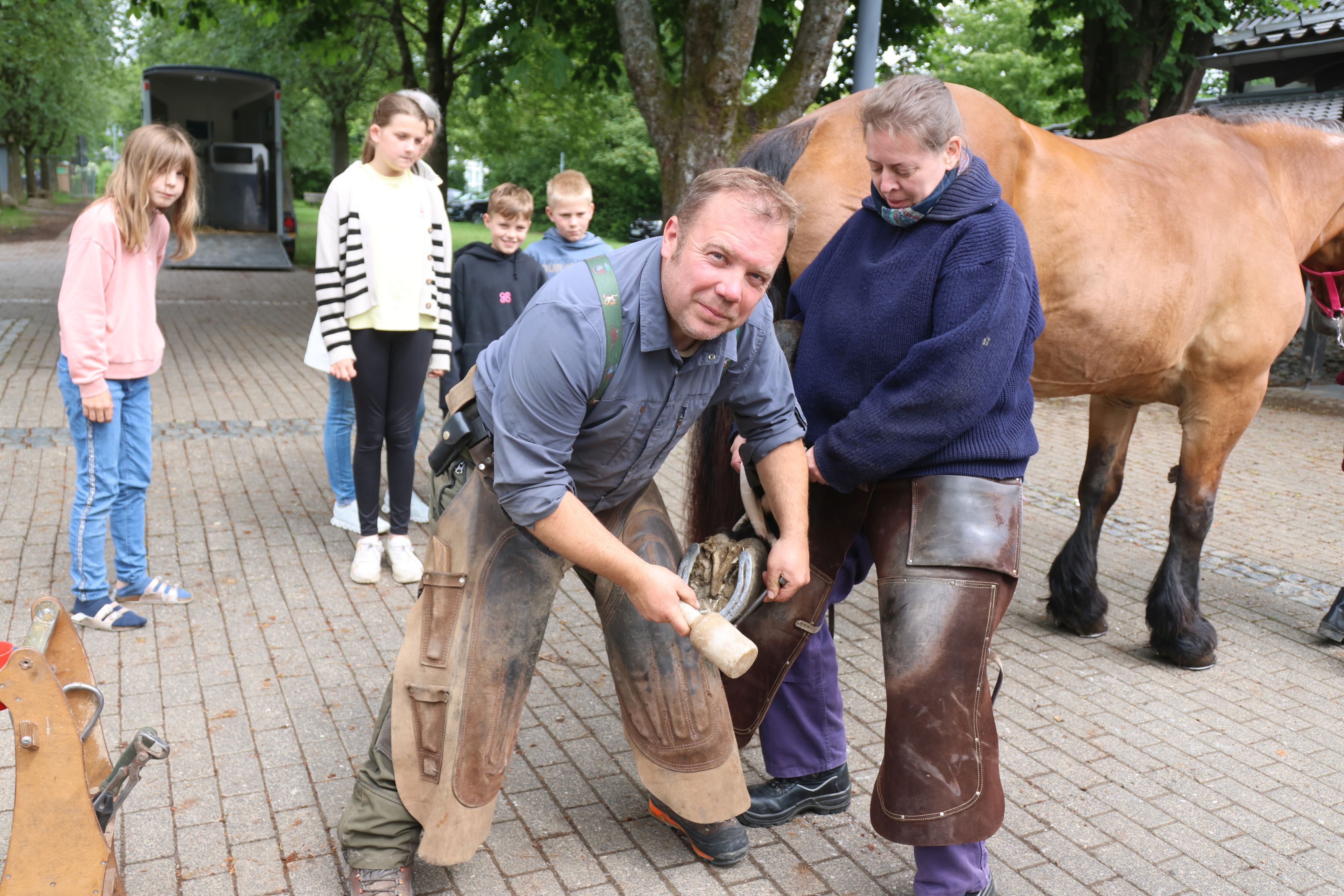 So geht’s: Roman Eßer setzt die Hufnägel, während Maja Laschinski den Hinterlauf hält. Und die Kinder von der Grundschule in Nümbrecht-Marienberghausen sehen fasziniert dabei zu.
