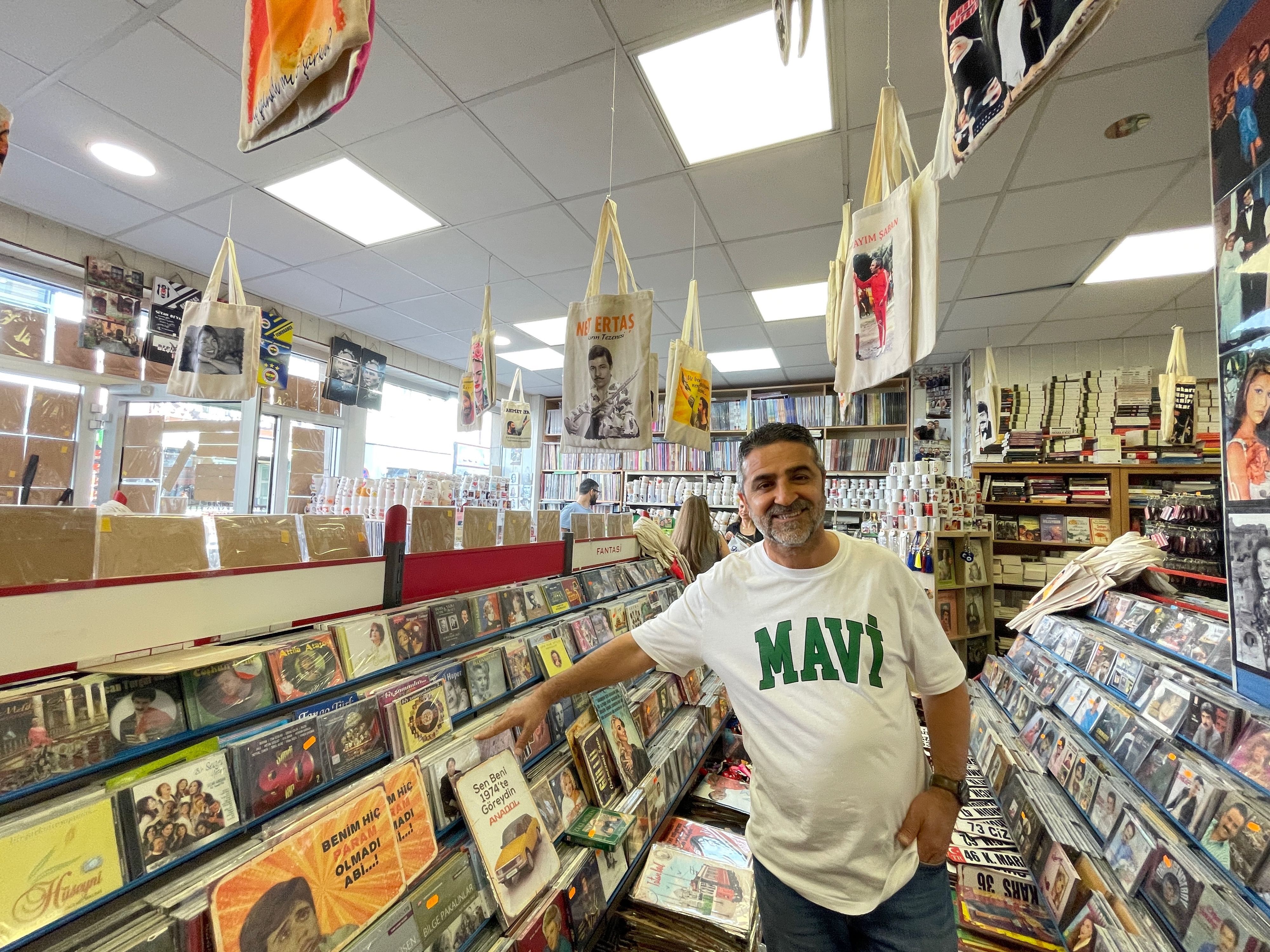 Ein Mann mit dunklem Haar und Dreitagebart steht zwischen Regalen voller Schallplatten und CDs.