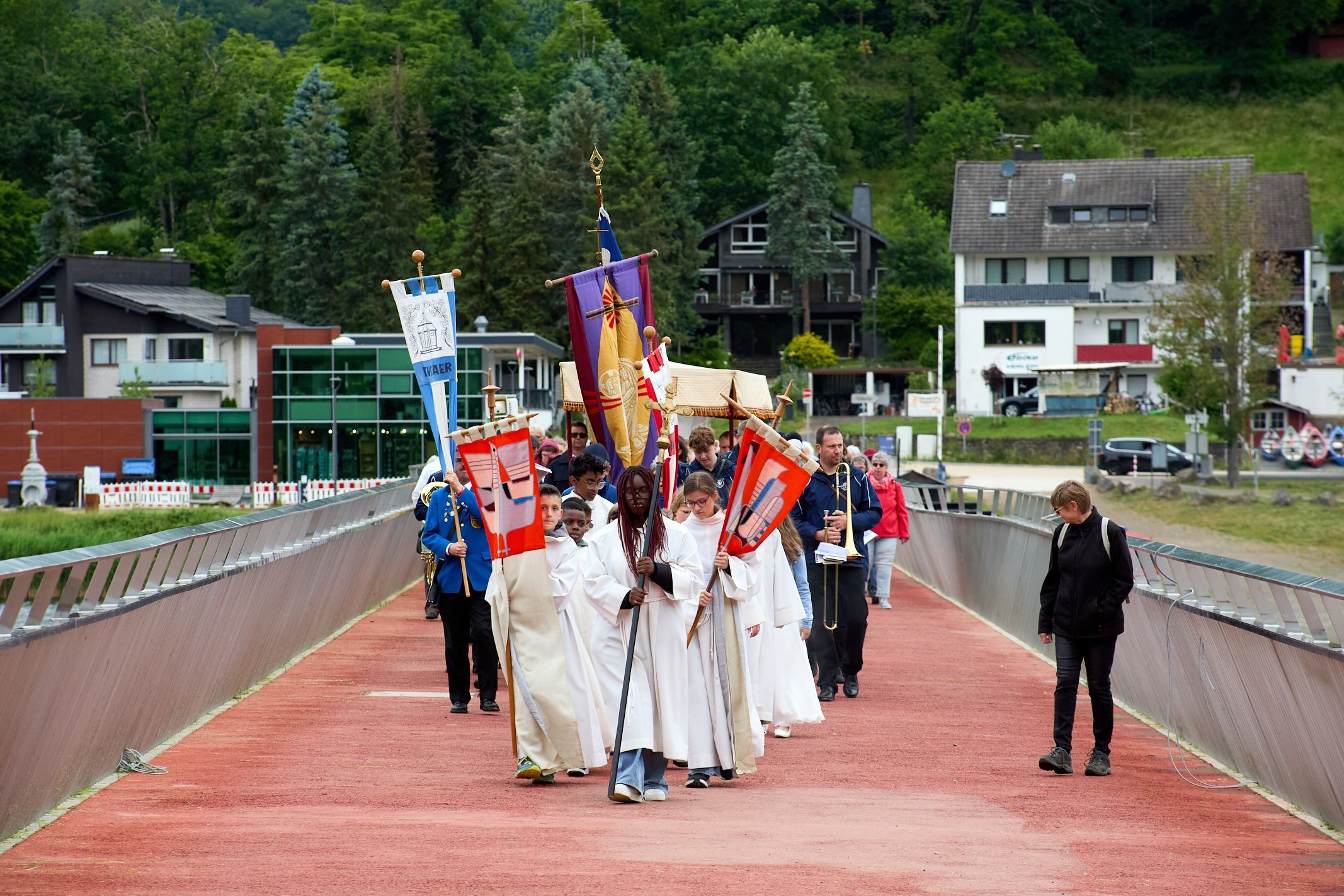 Ein Gruppe Messdienerinnen und Messdiener zieht mit Fahnen vor einer Menschengruppe über eine Brücke.