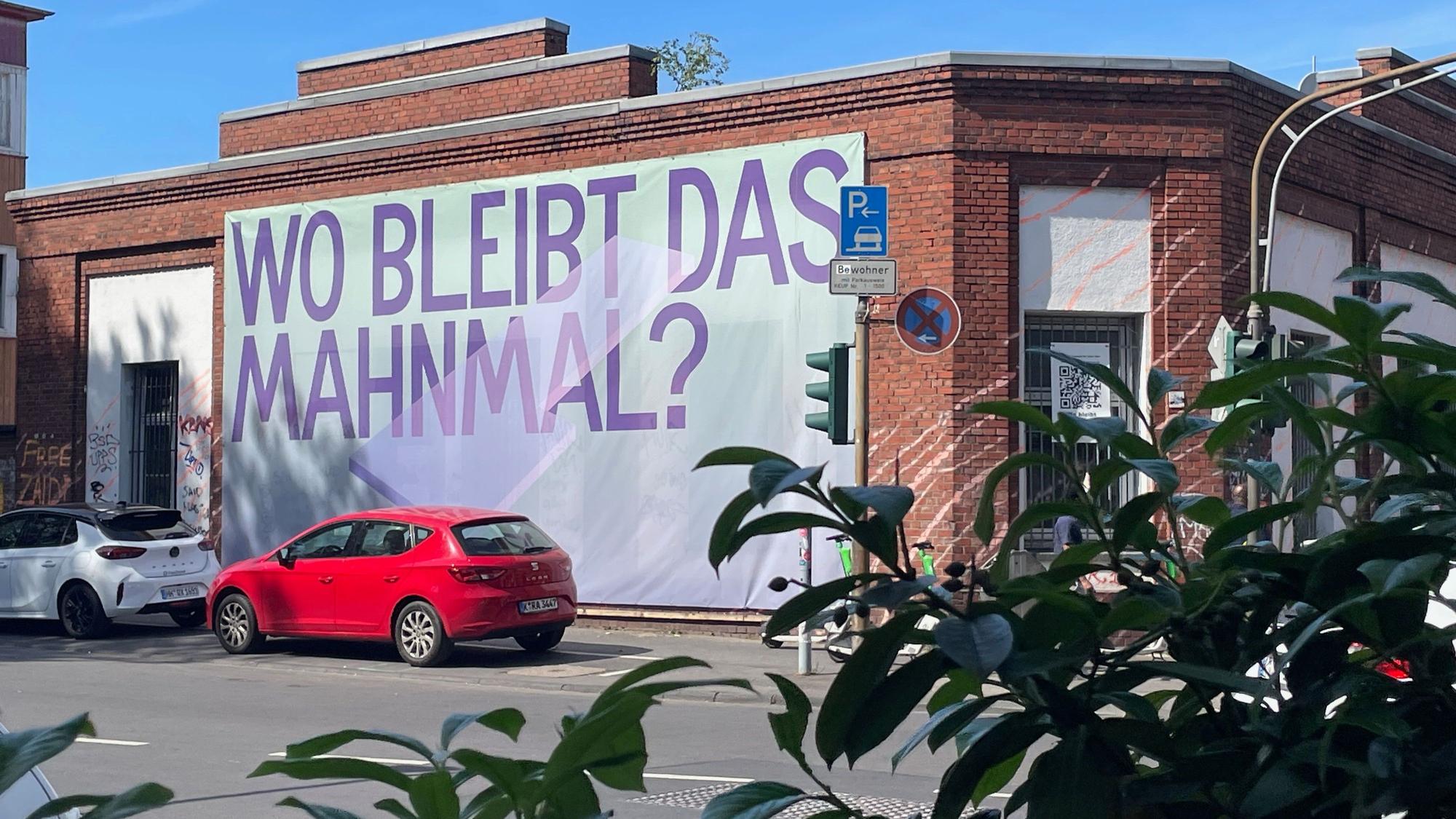 An der Backsteinfassade an einer Häuserecke hängt ein riesiges Banner: Wo bleibt das Mahnmal?
