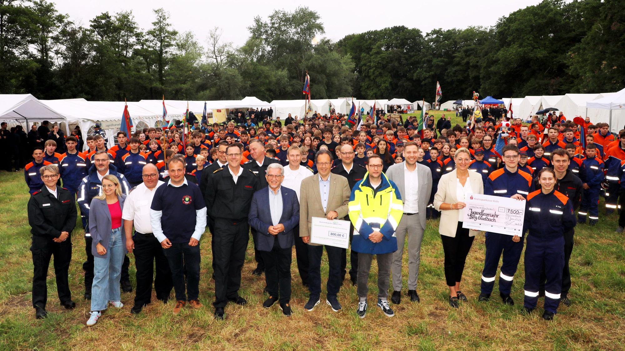 Kinder, Jugendliche und Betreuer von Jugendfeuerwehr und THW stehen mit Vertretern von Feuerwehr, Politik und Förderern auf dem großen Zeltlagerplatz des Kreisjugendfeuerwehrzeltlagers..