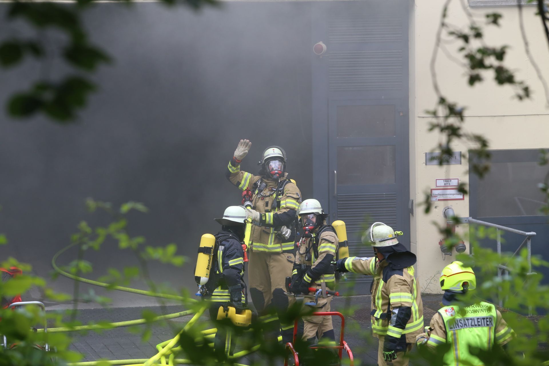 Rauch dringt aus einem Gebäude, davor Feuerwehrleute mit Atemschutzgeräten.