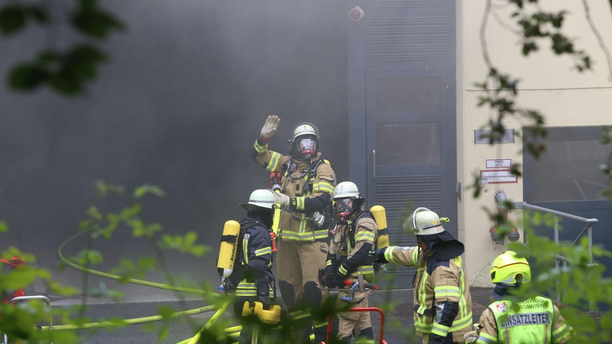 Rauch dringt aus einem Gebäude, davor Feuerwehrleute mit Atemschutzgeräten.