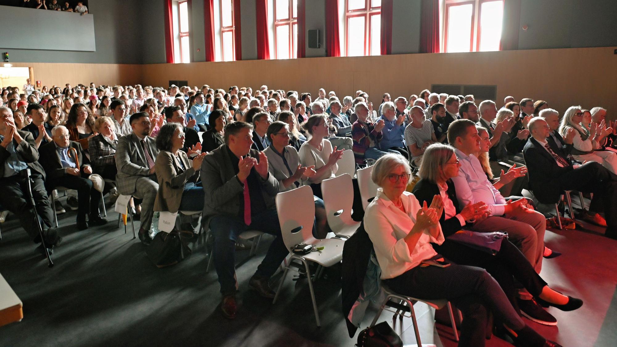 Zahlreiche Menschen sitzen auf Stühlen in der Aula der Gesamtschule Euskirchen und applaudieren.
