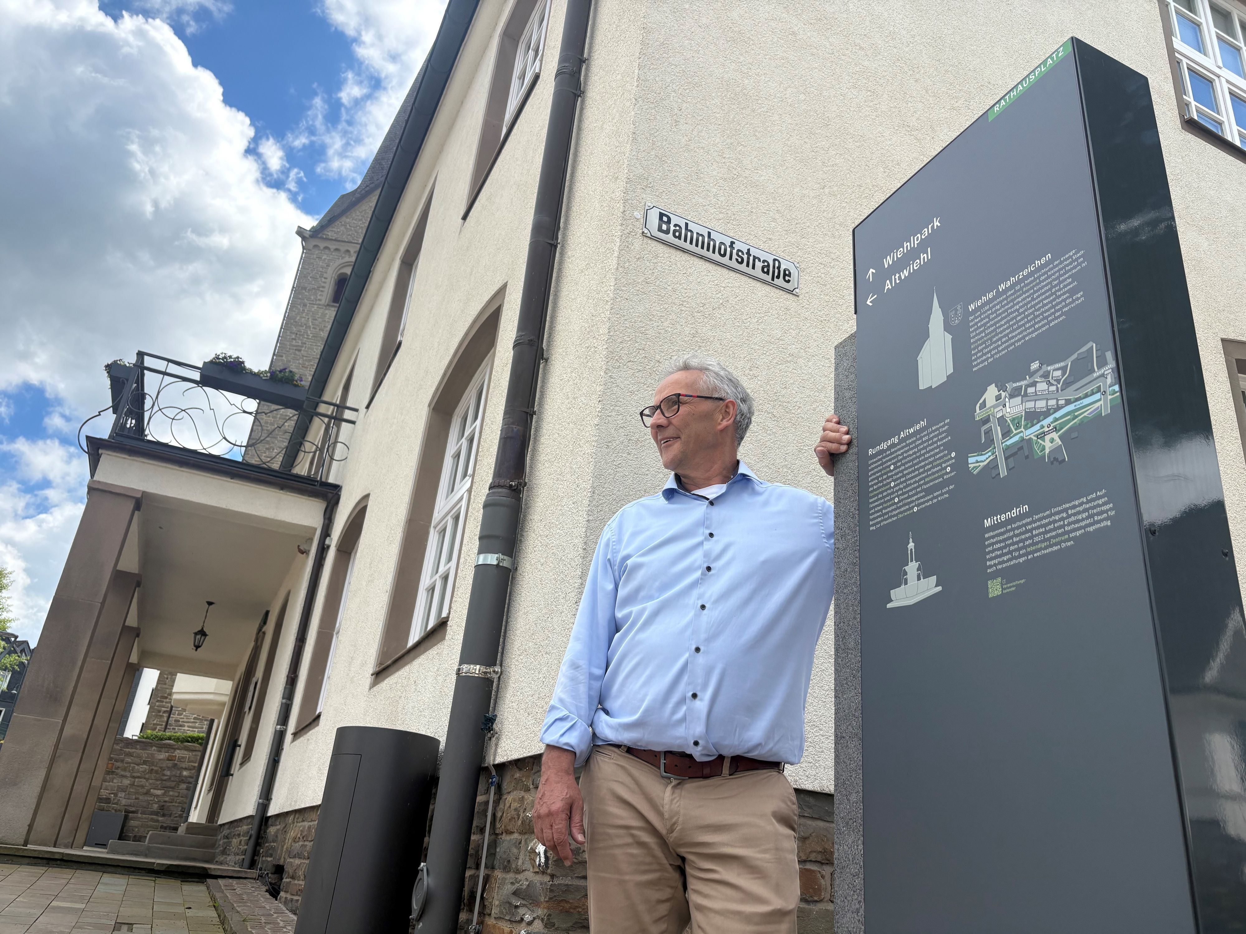 Ein Mann lehnt an einem Schild vor dem Rathaus Wiehl.