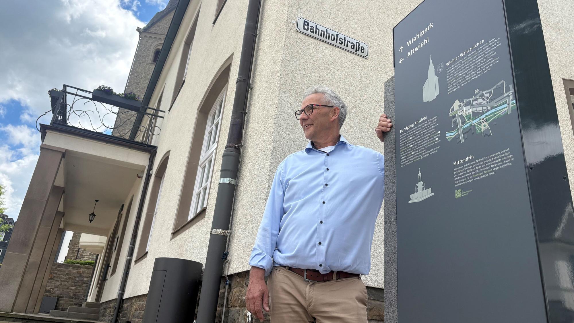Ein Mann lehnt an einem Schild vor dem Rathaus Wiehl.